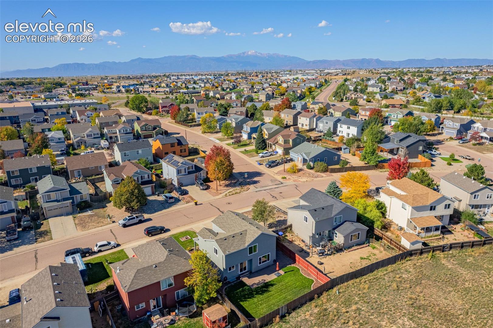 Aerial perspective of a suburban neighborhood featuring a mountain backdrop, multi-story residences, fenced rear yards, and established landscaping