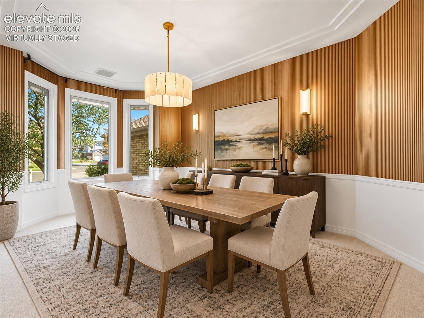 Dining area featuring vertical wood-slat wall paneling, crown molding, a bay window configuration, and an integrated drum pendant light fixture- virtually staged