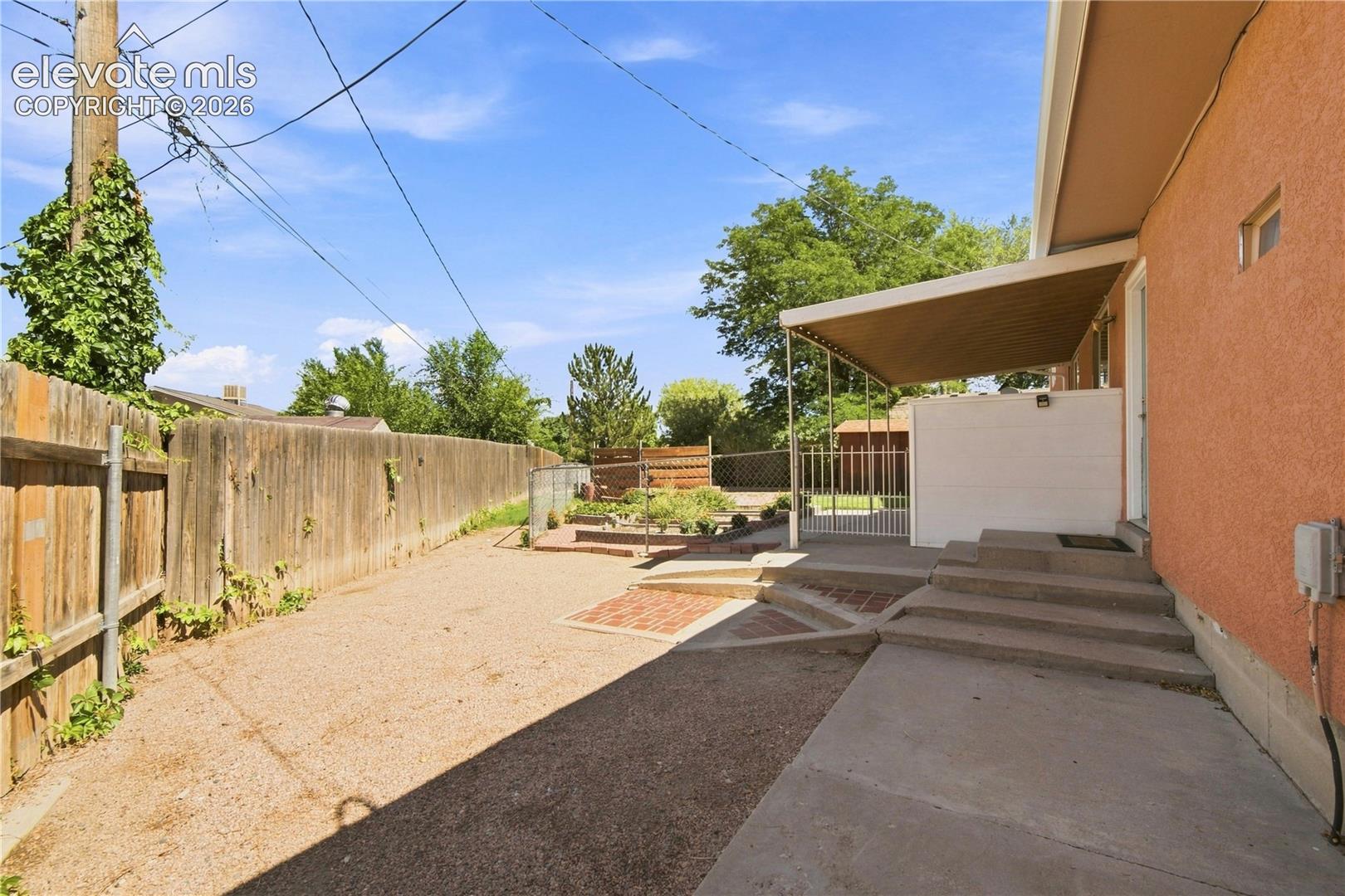 Expansive rear yard featuring a wood privacy fence, gravel surface, and concrete steps leading to a covered patio