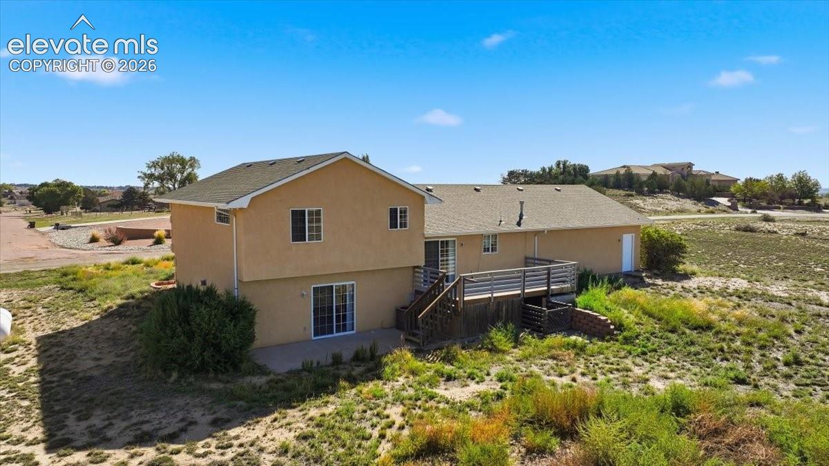 Stucco exterior with a multi-level deck featuring wood railings, a ground-level patio, and sliding glass doors