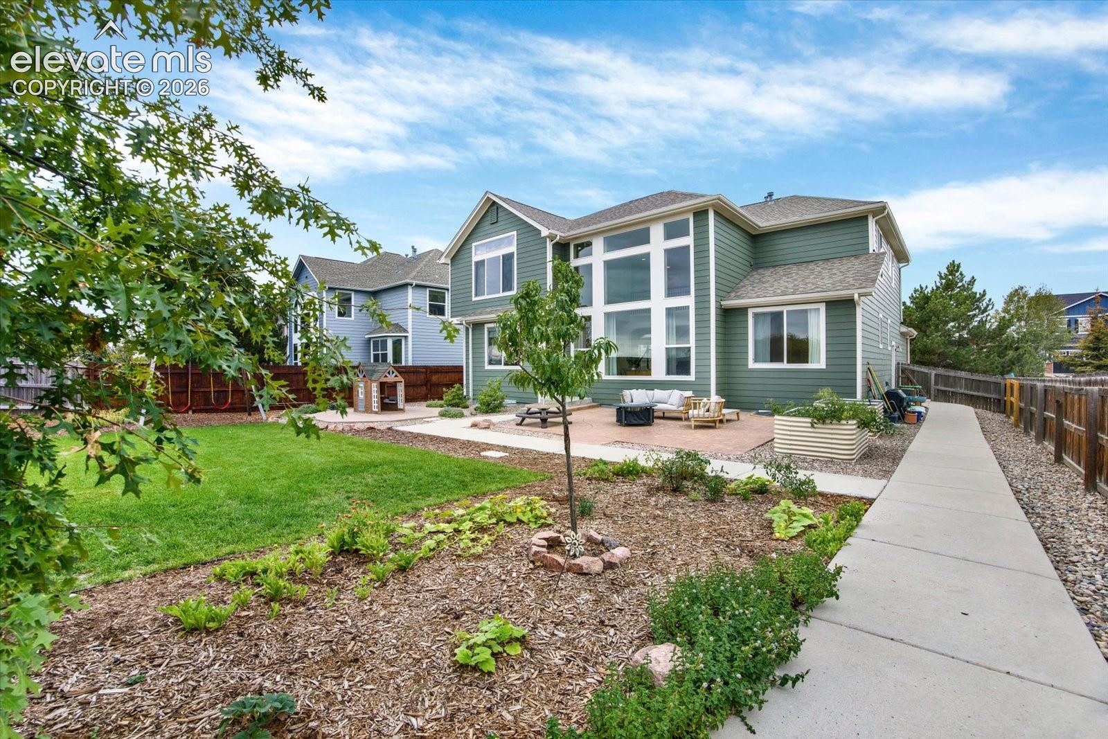 Two-story exterior with horizontal siding and floor-to-ceiling windows, featuring a stone-paver patio, manicured lawn, and perimeter wood fencing