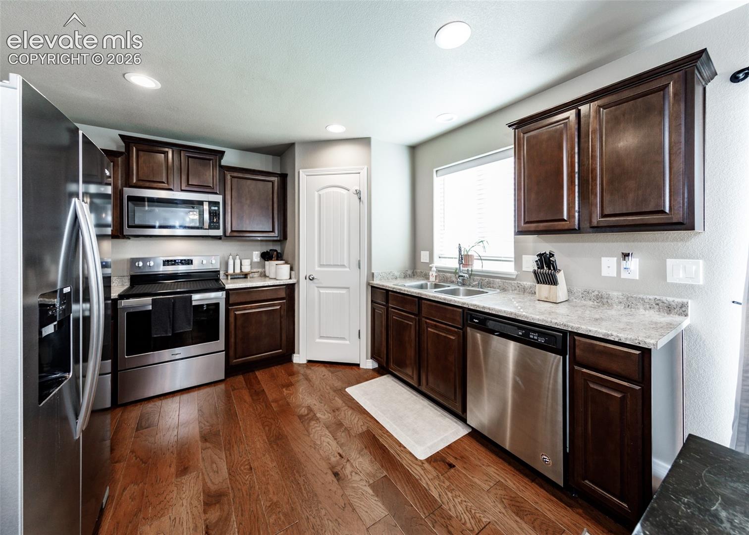 Kitchen featuring dark-finish cabinetry, stainless steel appliances, neutral countertops, wood-finish flooring, and recessed lighting