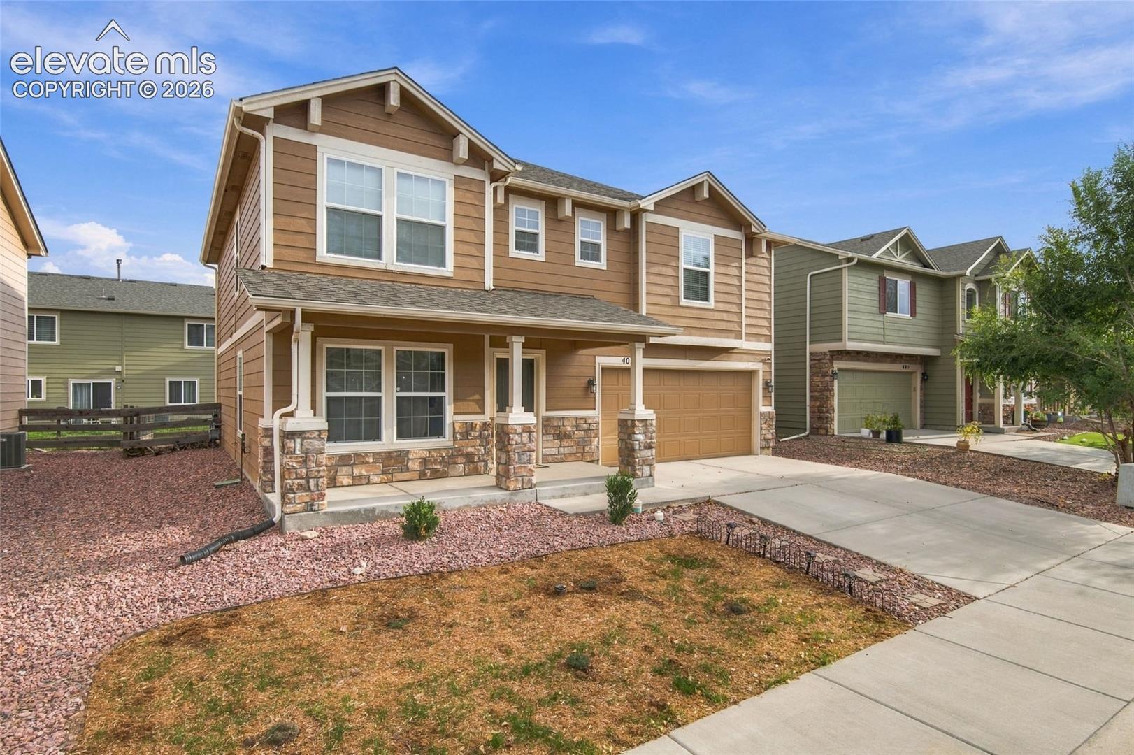Two-story residence featuring horizontal lap siding, stone veneer accents, a covered front porch with column supports, and an attached two-car garage