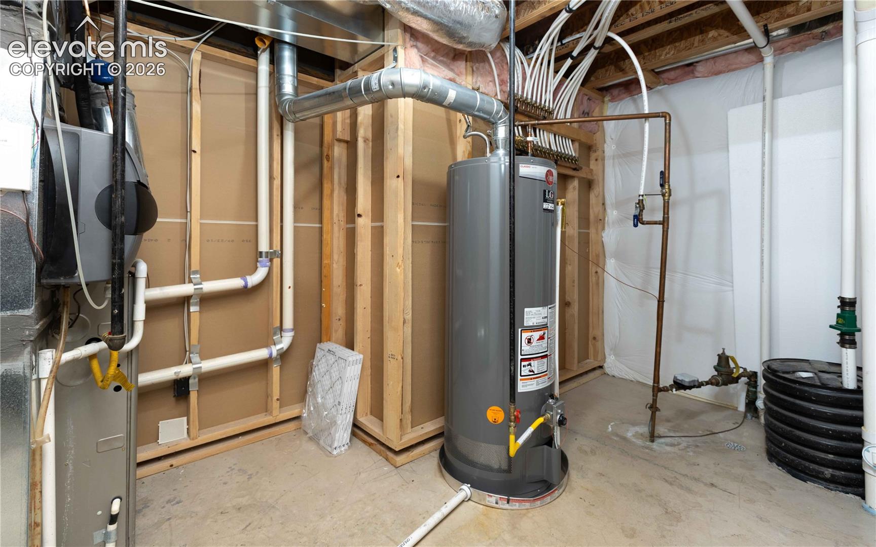 Mechanical area featuring a vertical water heater, exposed wood framing, interior wall insulation, copper plumbing lines, and a manifold distribution system