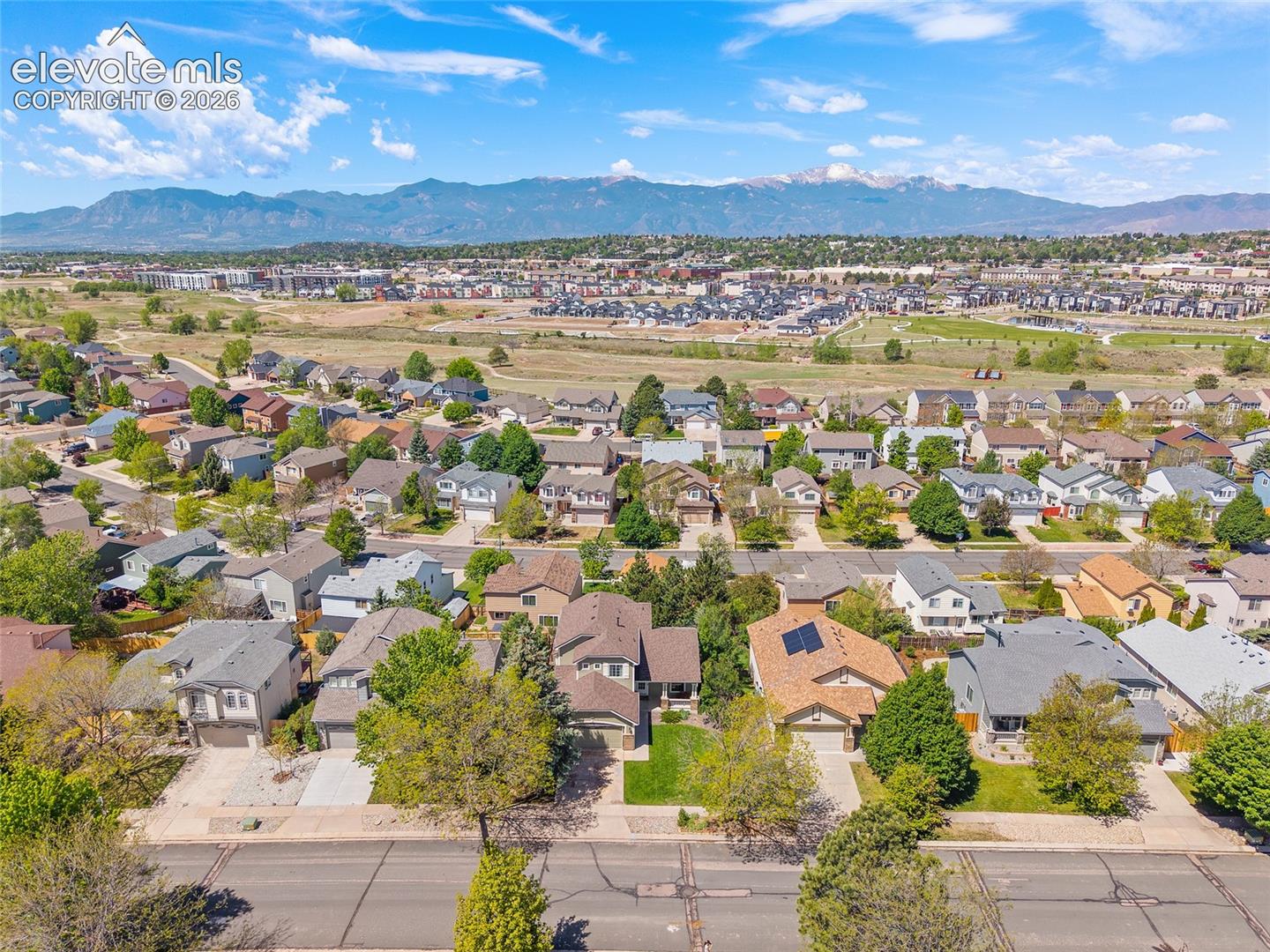 Expansive neighborhood aerial showcasing residential properties with mature trees and mountain scenery