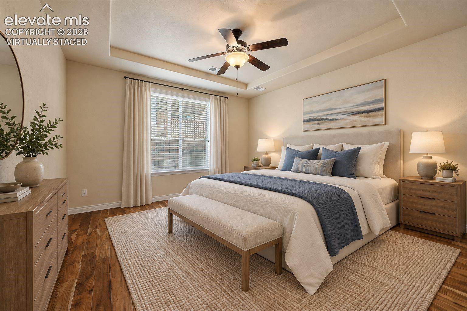 Virtually staged. Room featuring wood-finish flooring, a recessed tray ceiling, and a central ceiling fan with integrated lighting