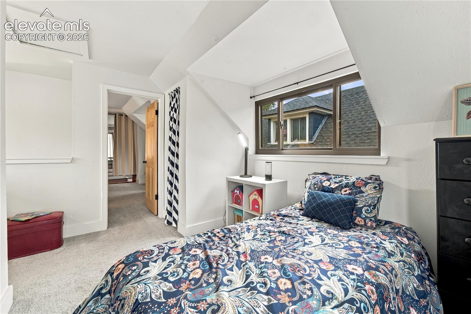 Sloped ceiling room featuring wall-to-wall carpeting, a dormer window with dark-toned frames, and a solid wood interior door