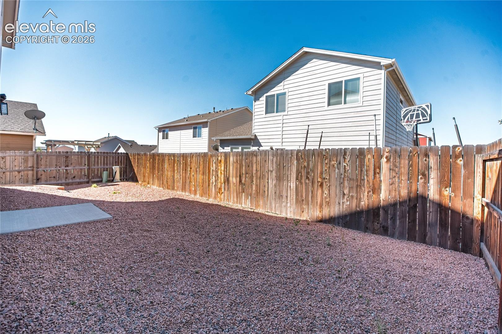 Expansive backyard featuring a gravel surface, wood privacy fencing, and a concrete pad
