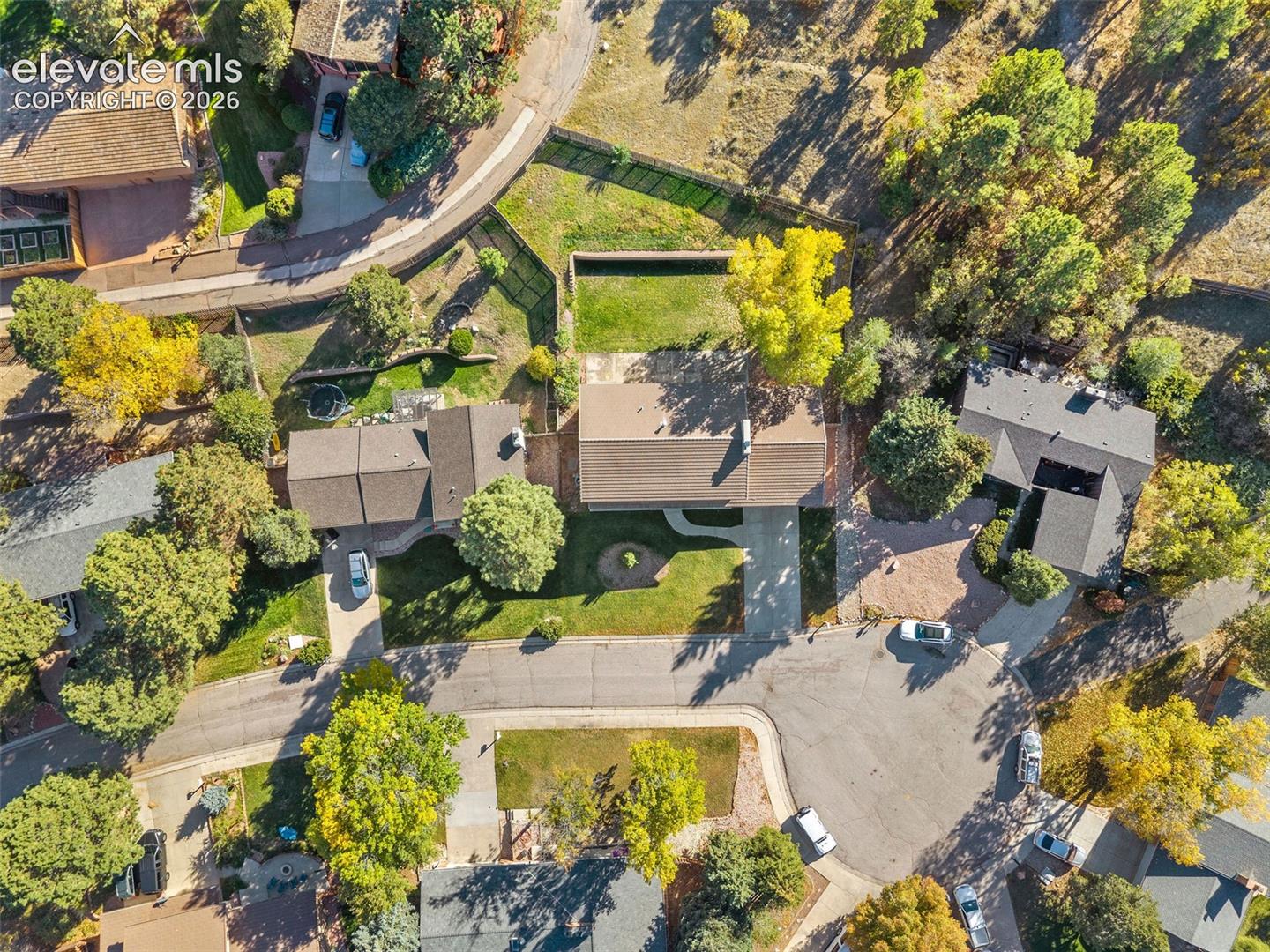 Aerial perspective of the home featuring a concrete driveway, multi-gabled rooflines, a grass lawn, and mature trees on a cul-de-sac backing to open space.