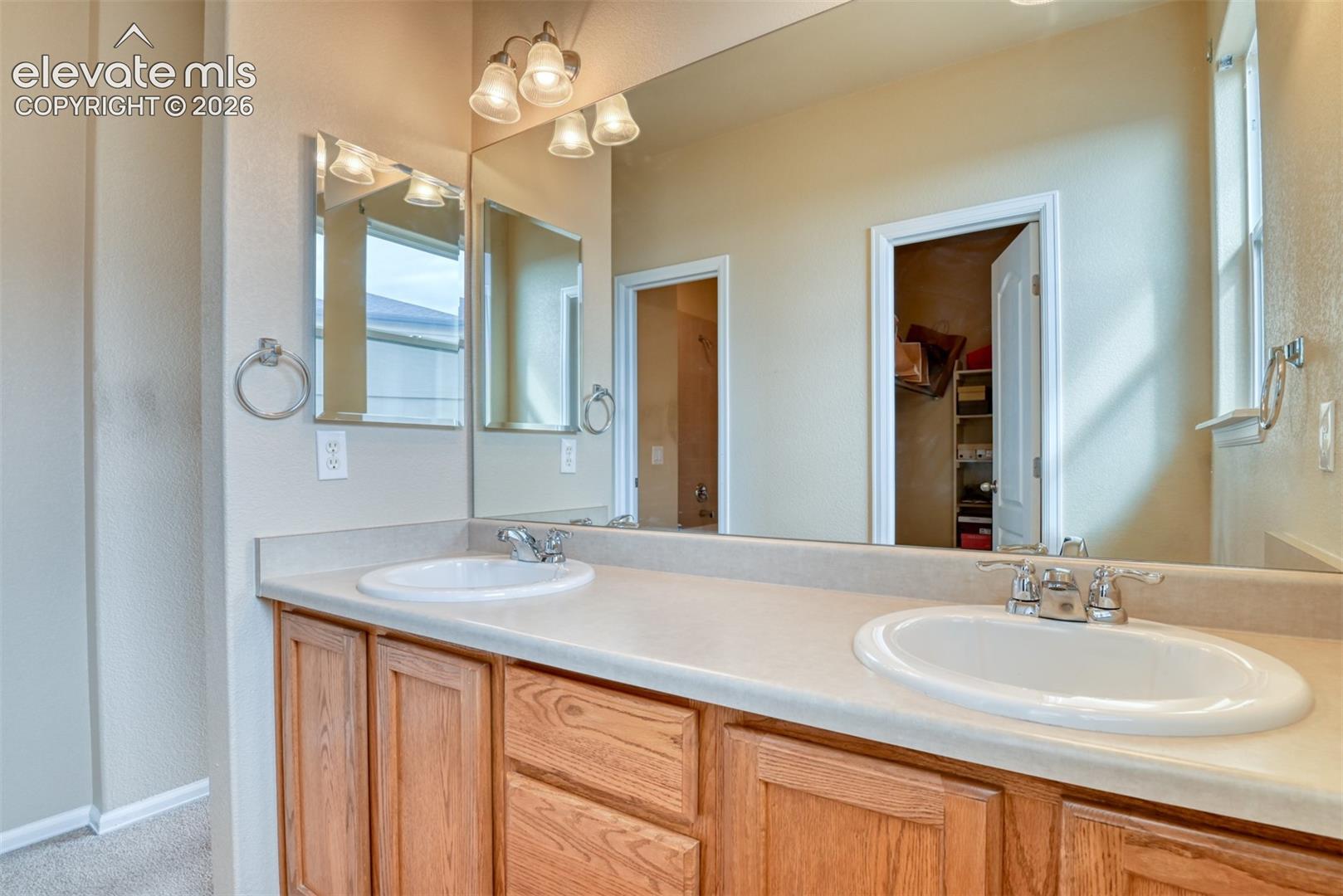 Dual-sink vanity with a solid-surface countertop, wood cabinetry, large vanity mirror, and three-light decorative fixture