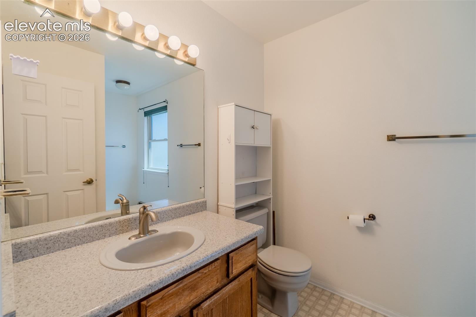Vanity with a single basin sink, speckled countertop, and wood-finish cabinetry