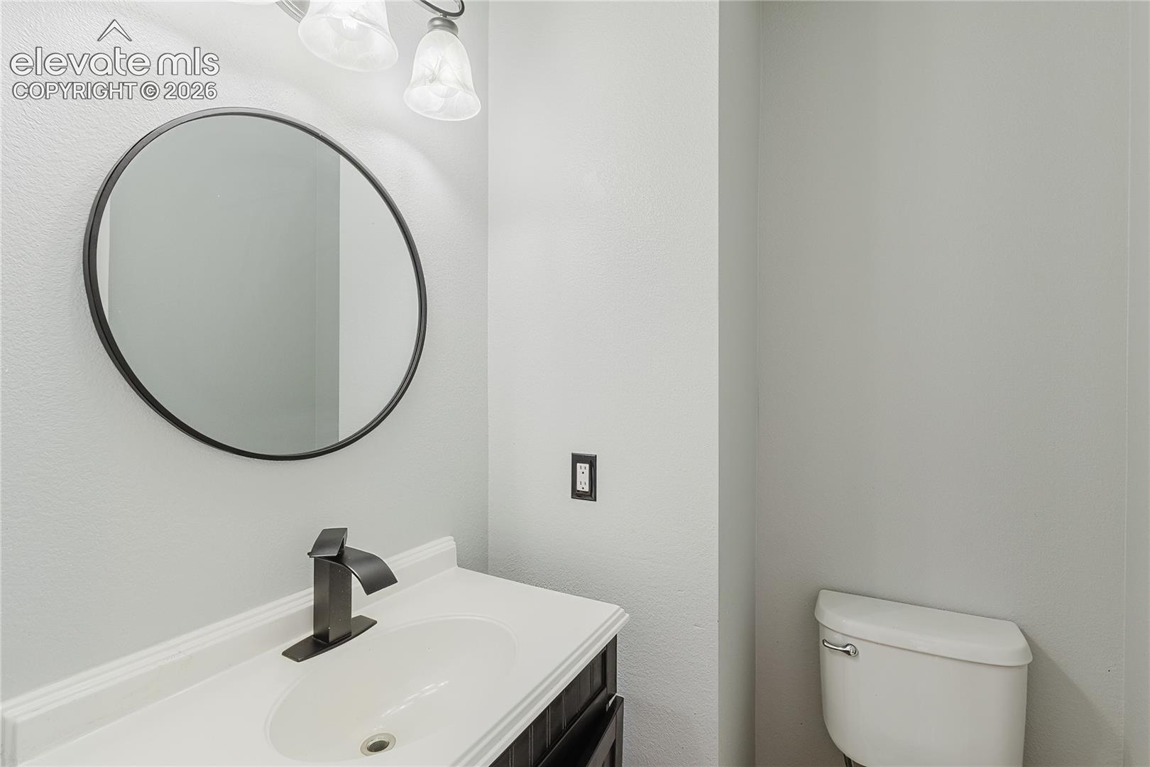Modern bathroom featuring a circular framed mirror with matte black finish, white porcelain rectangular vessel sink, matte black wall-mounted faucet, and white subway tile walls