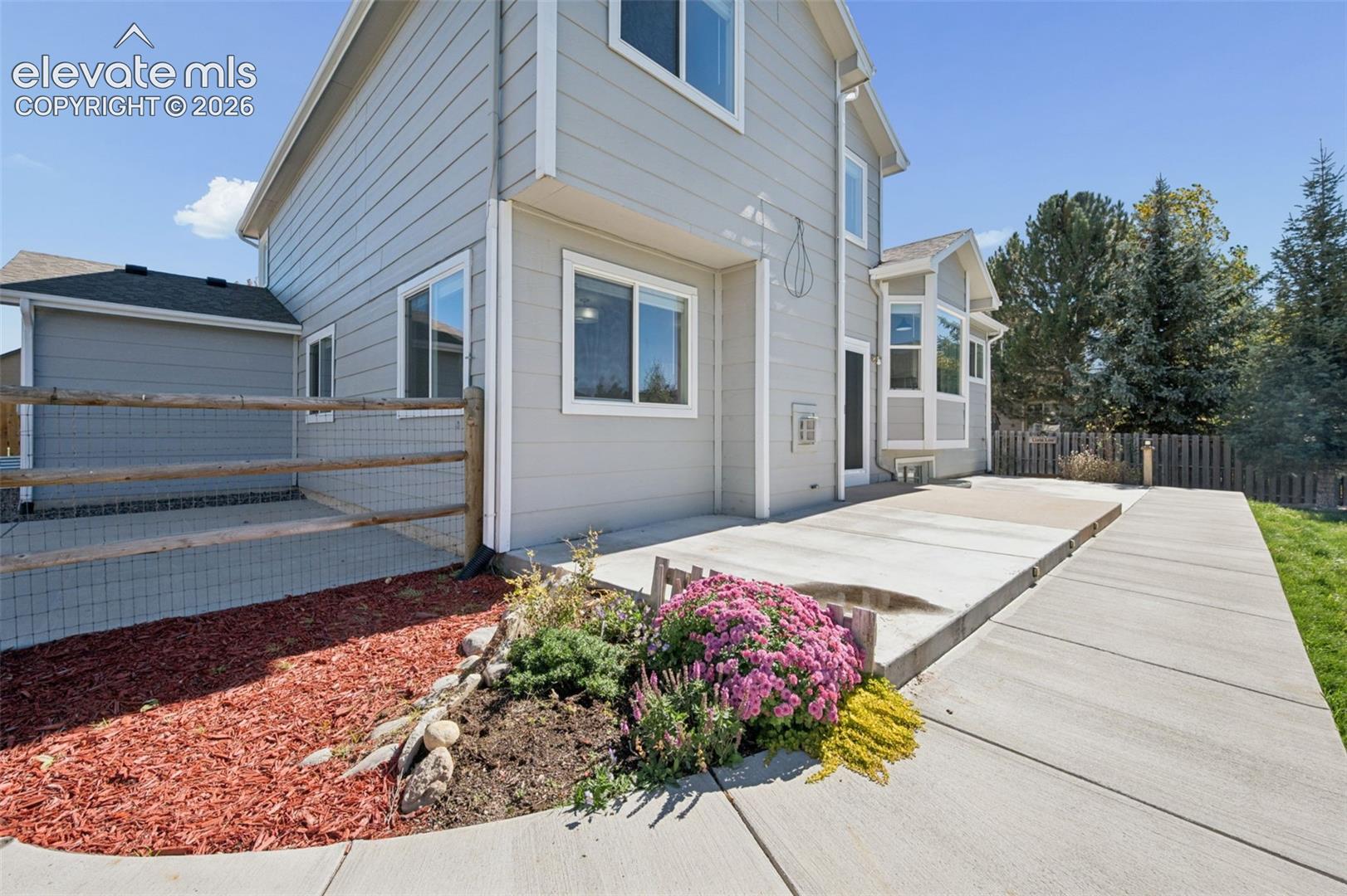 Exterior featuring horizontal siding, concrete patio, split-rail fencing, and low-maintenance landscaping with rock mulch and floral shrubbery