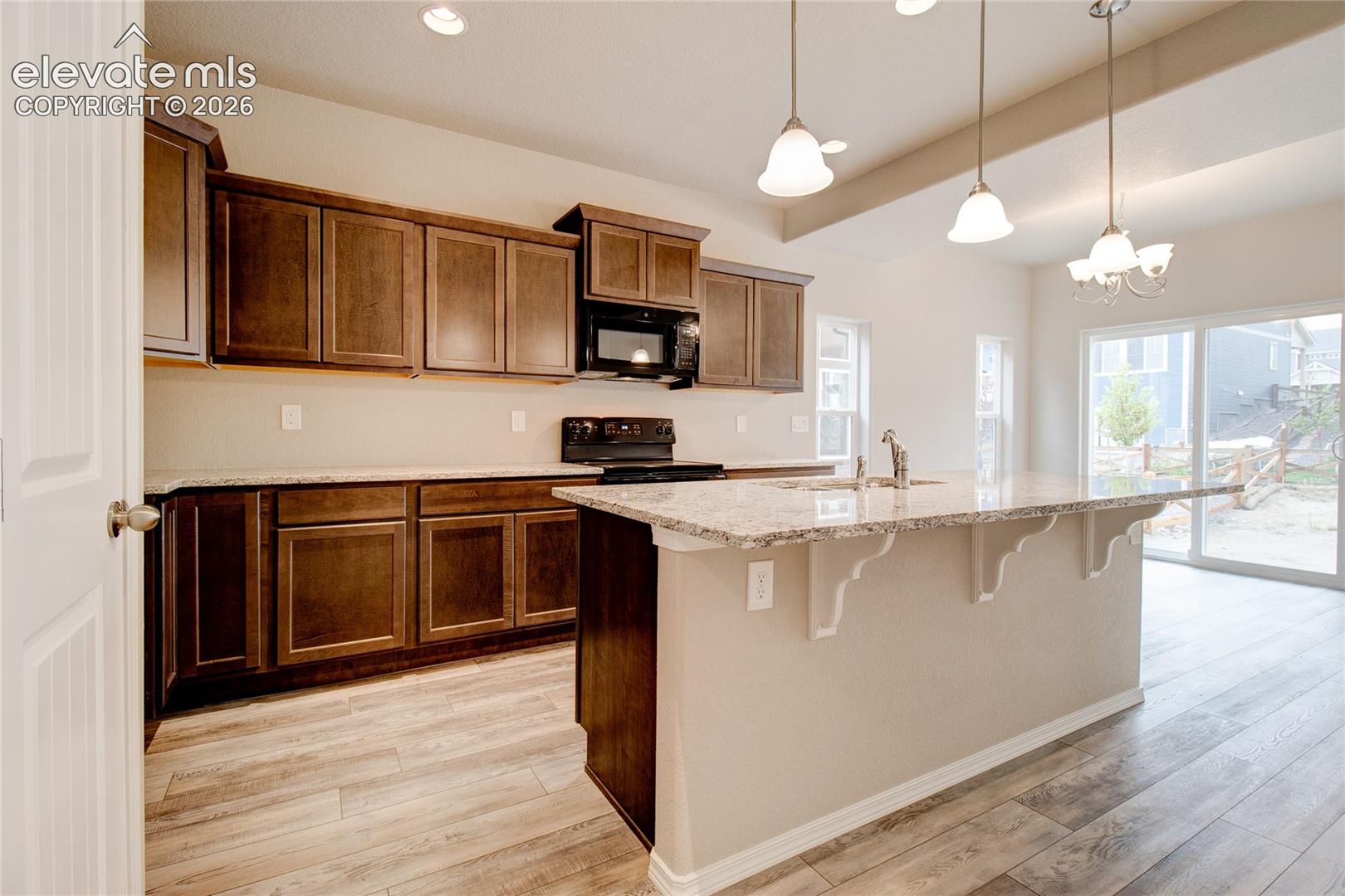 Kitchen featuring shaker-style cabinetry, stone-finish countertops, a central island with decorative corbels, wood-finish flooring, and recessed and pendant lighting