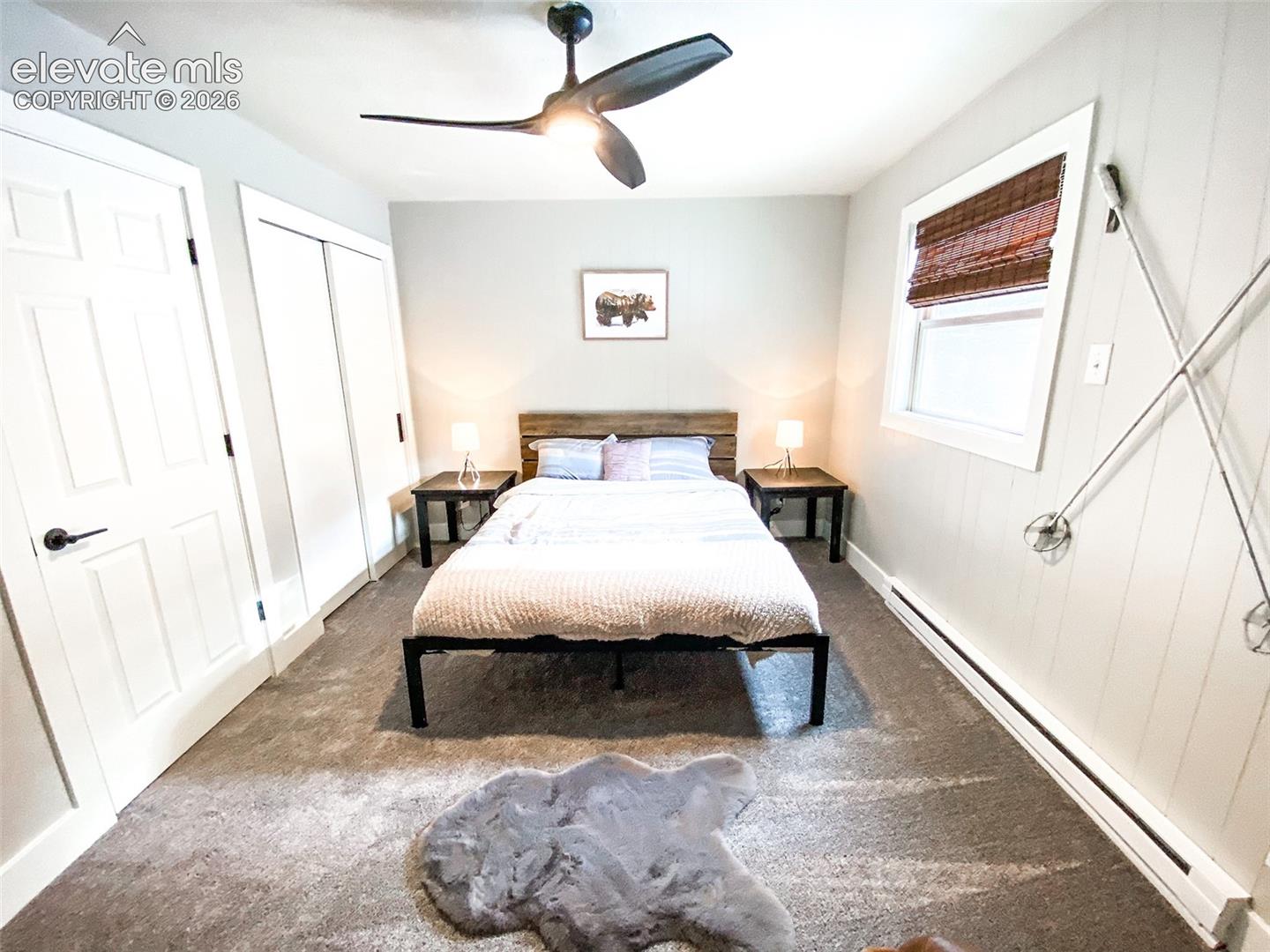 Bedroom featuring a wood-panel accent wall, carpeted flooring, and a ceiling fan with integrated lighting