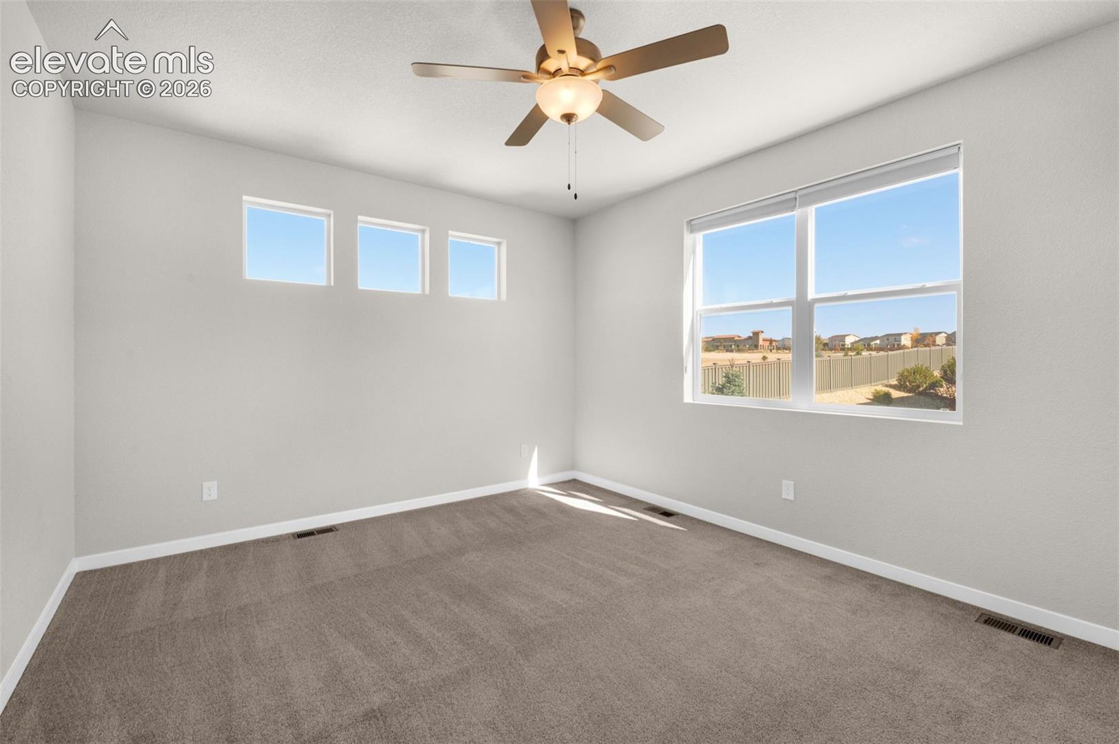 Neutral-toned room featuring wall-to-wall carpeting, three high-set square windows, a large double-pane window, and a ceiling-mounted light fixture with a fan