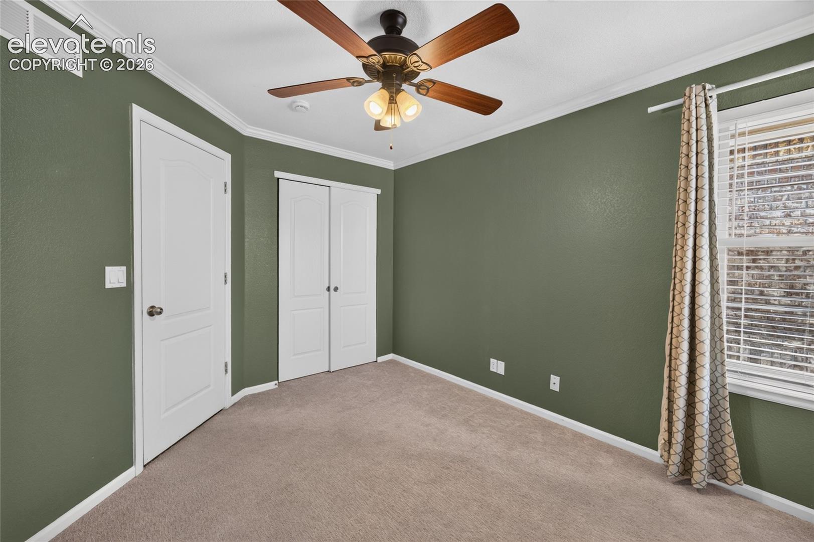 Bedroom featuring neutral-toned carpeting, crown molding, double-panel interior doors, and a ceiling fan with integrated lighting