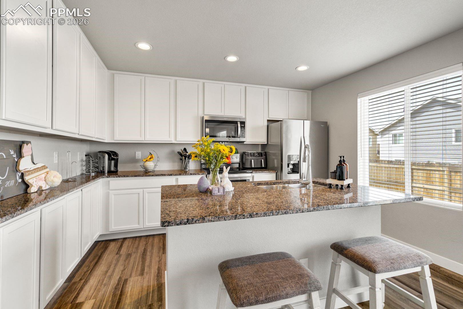 Kitchen featuring white cabinetry, dark wood-type flooring, dark stone counters, stainless steel appliances, and a kitchen bar