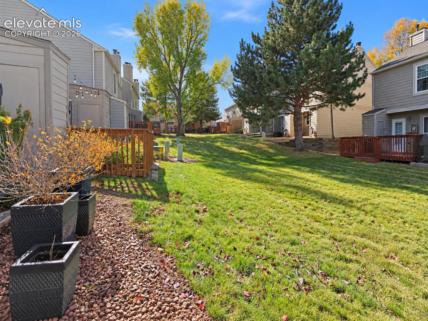 Expansive lawn featuring mature trees, wood-slat decks, and decorative stone landscaping borders
