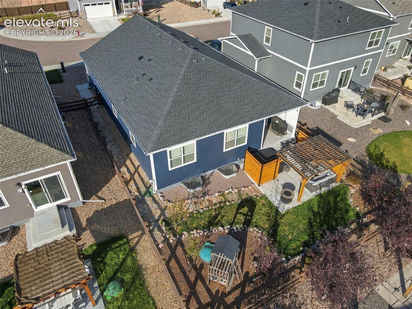 Rear exterior featuring a covered patio with a wooden pergola, concrete hardscaping, a grass lawn, and rock landscaping