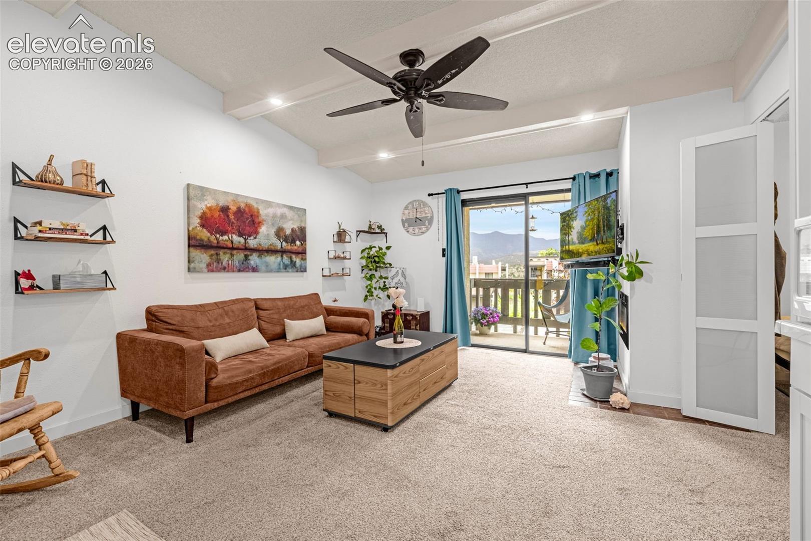 Recessed lighting illuminates the open living space, featuring a ceiling fan and exposed white beams