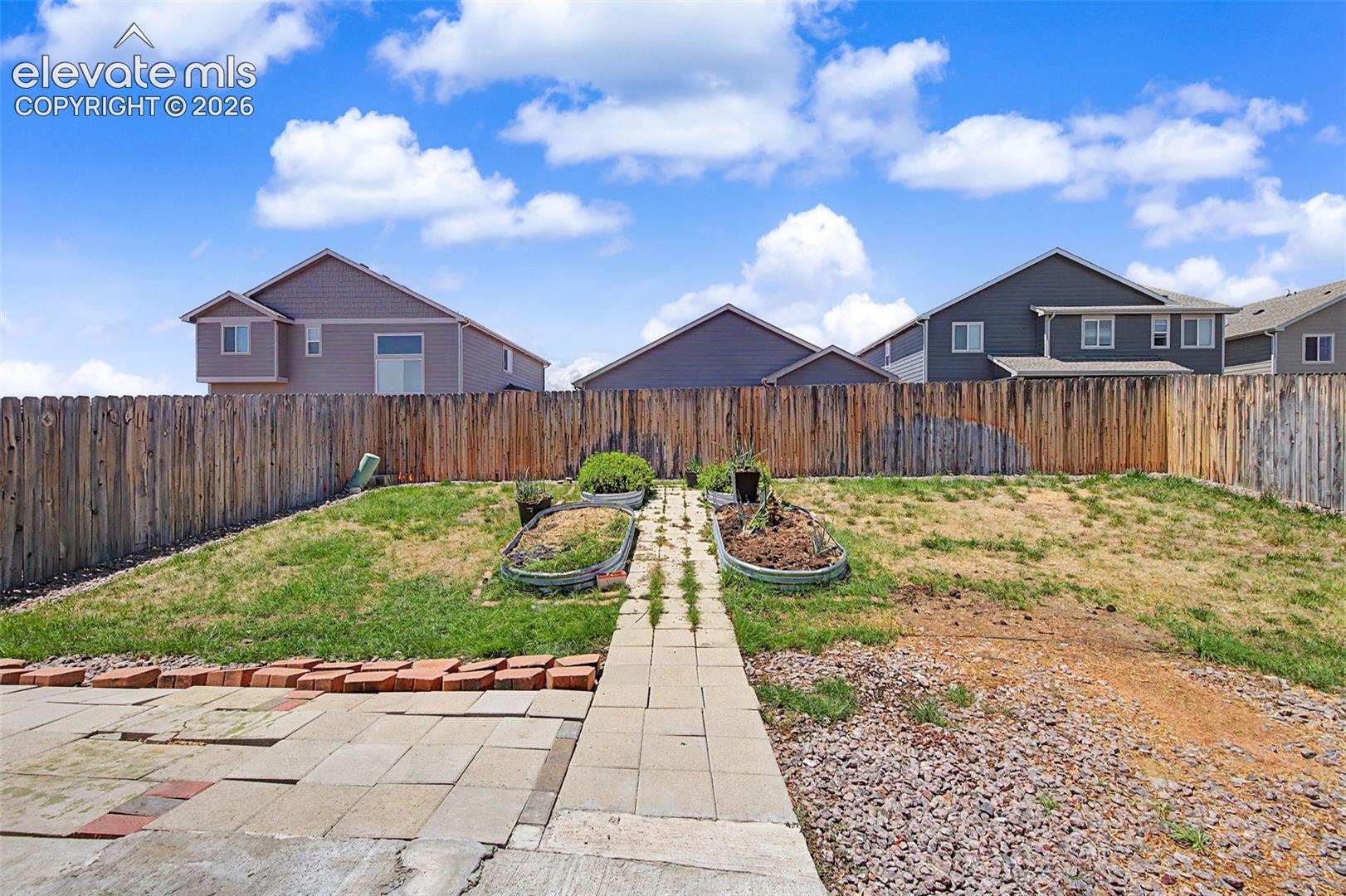 Spacious backyard featuring a wood privacy fence, a stone paver patio, a partial gravel area, and two raised garden beds with metal edging