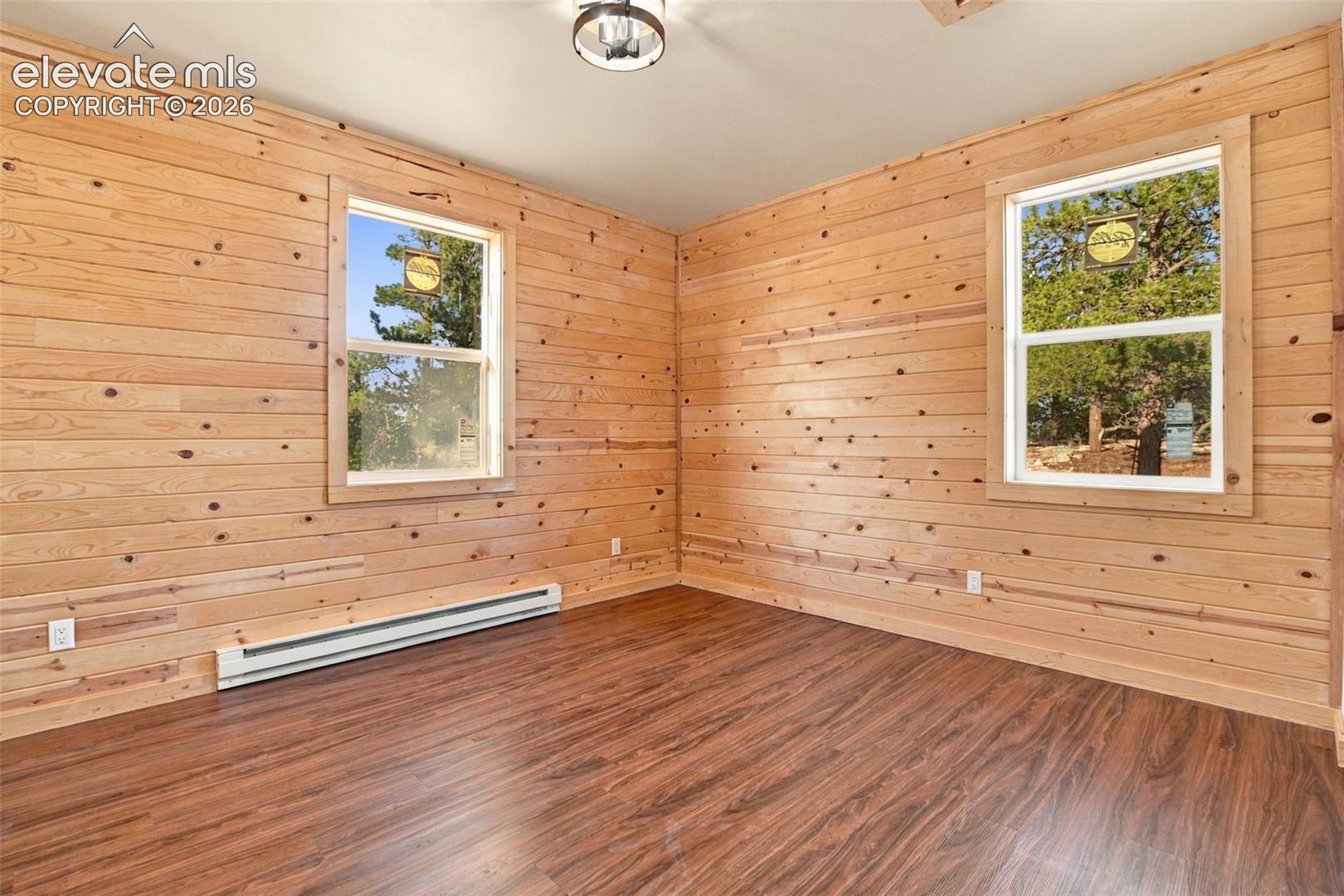 Interior space featuring natural knotty pine wall paneling, wood-finish flooring, two dual-pane windows, and a flush-mount industrial-style lighting fixture