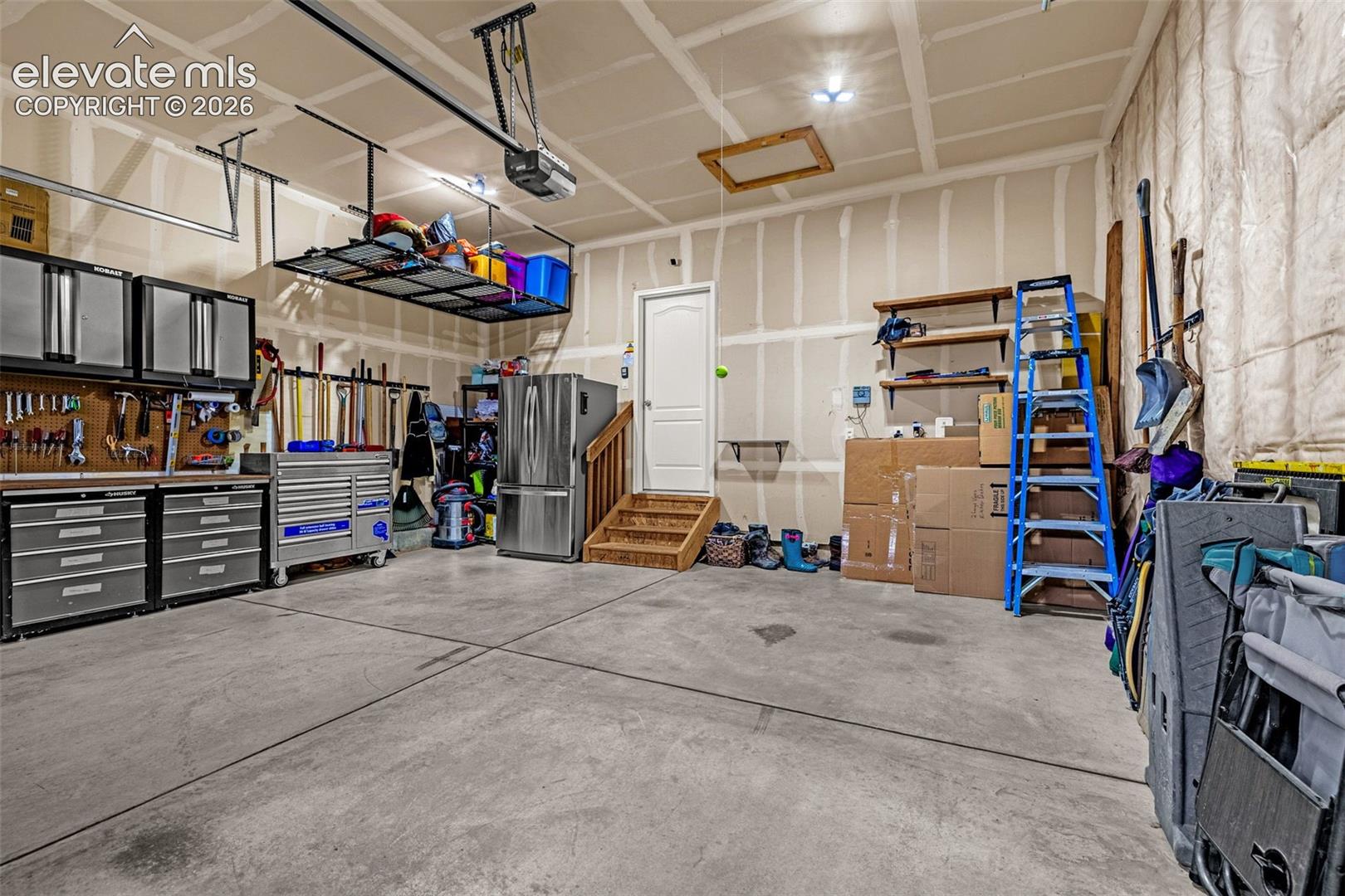 Finished garage interior featuring concrete flooring, ceiling-mounted storage racks, and built-in wall shelving