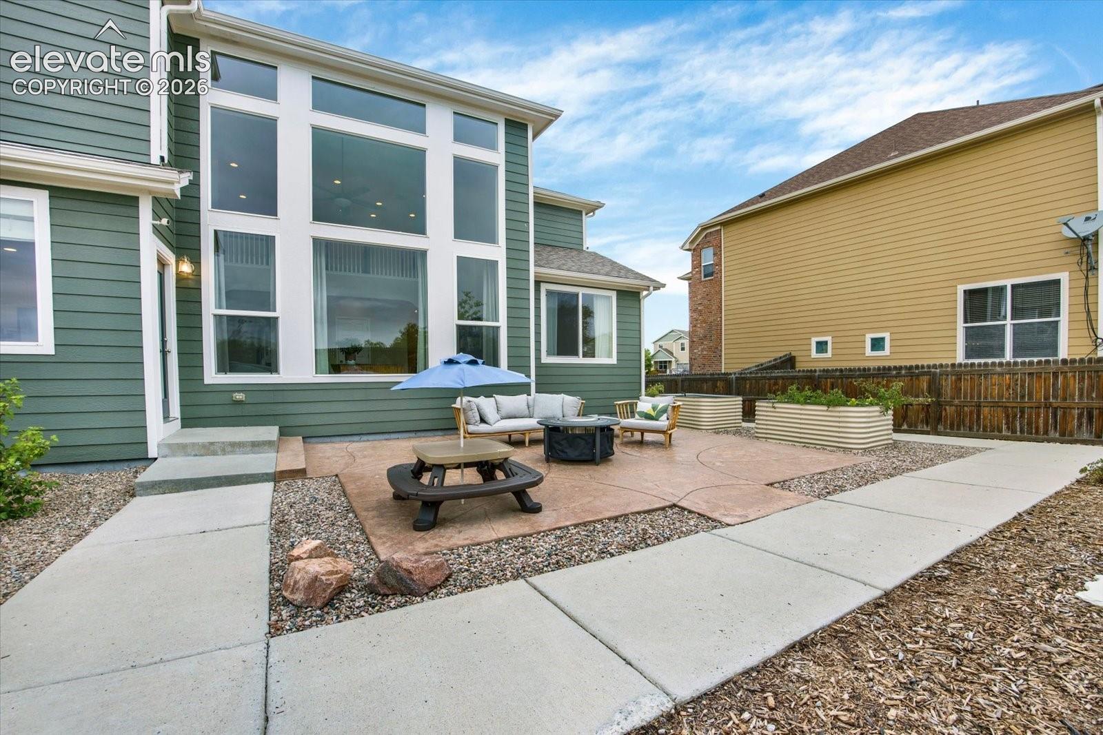 Rear exterior featuring multi-story windows, stamped concrete patio, metal raised garden beds, and wood privacy fencing
