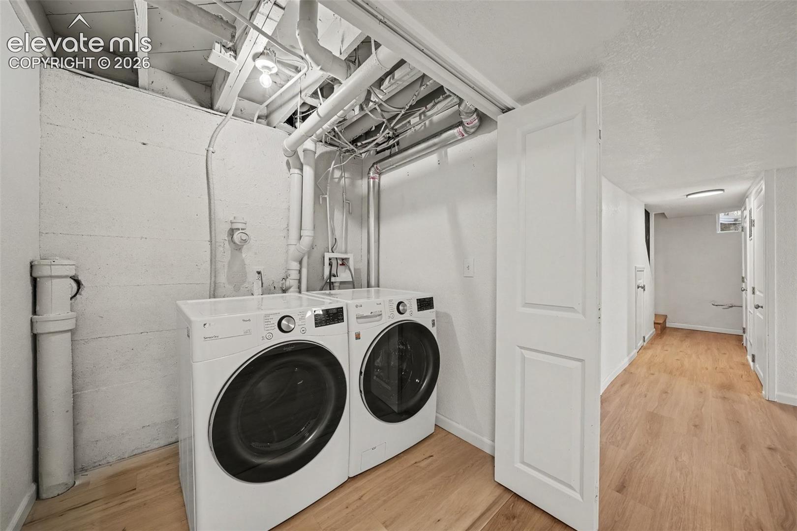 Utility area featuring wood-finish flooring, painted cinder block walls, exposed structural ceiling beams, and a white paneled door