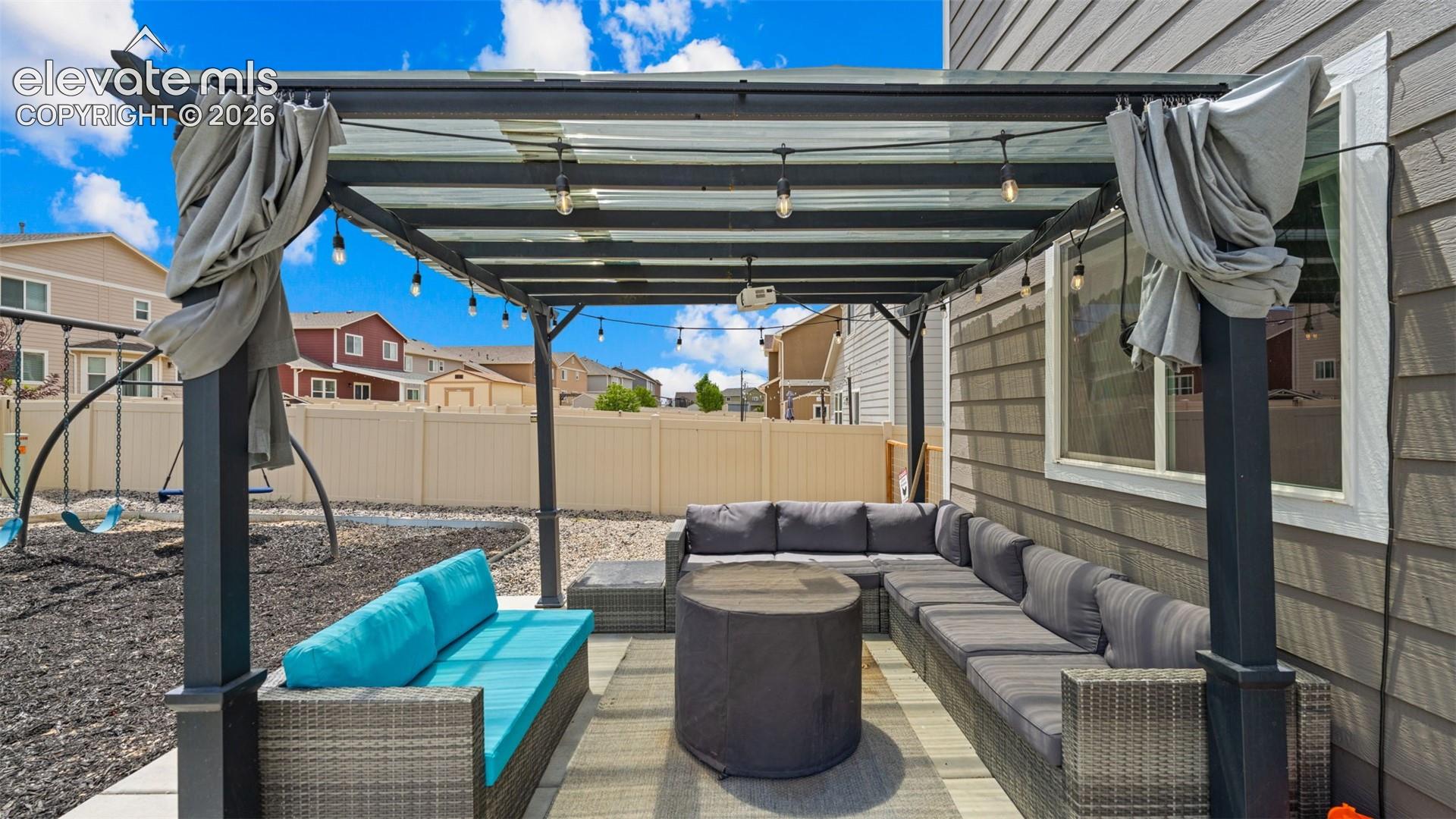 Outdoor patio featuring a black metal pergola with string lighting and draped fabric accents