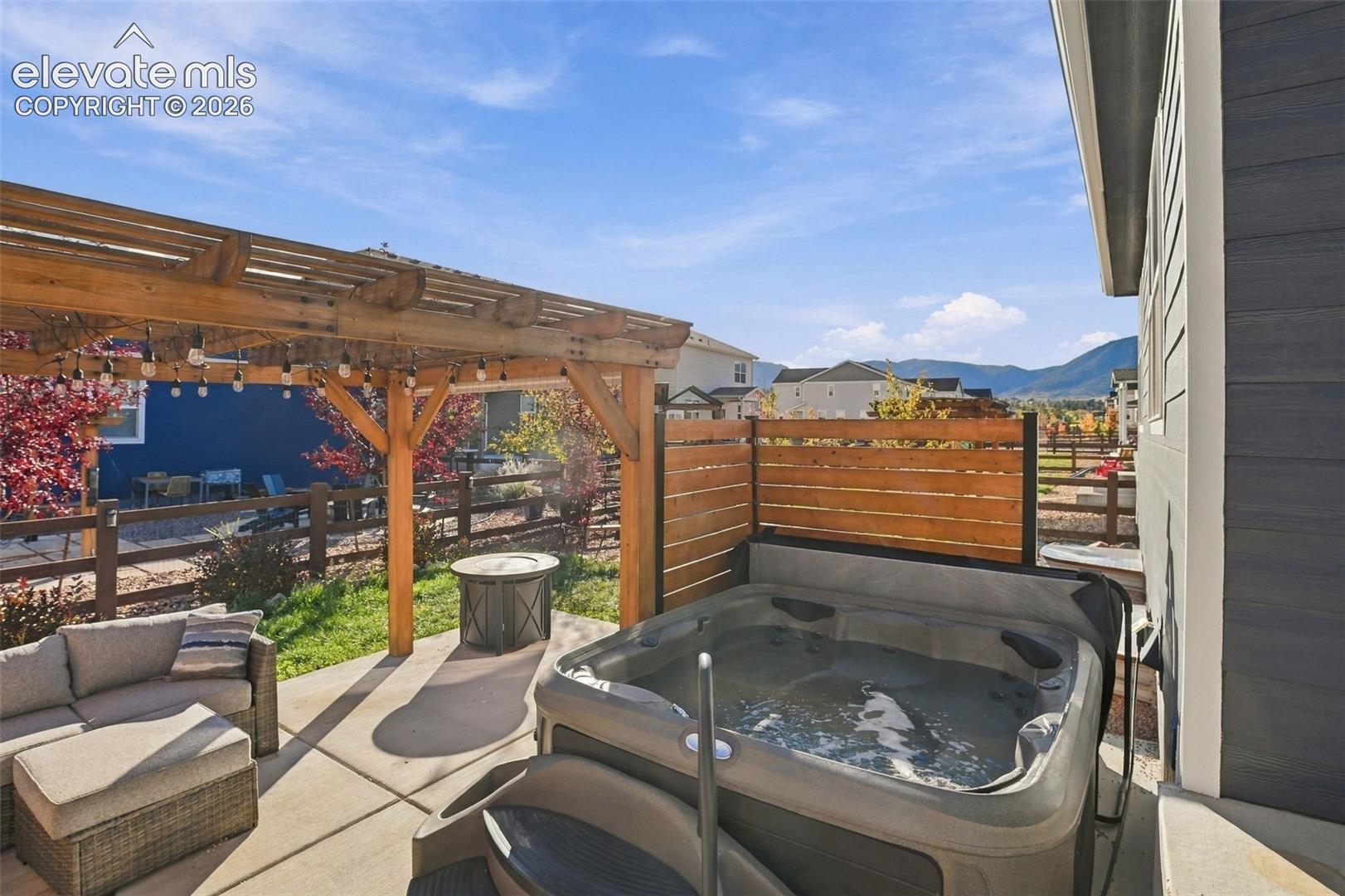 Rear patio featuring a wooden pergola, built-in hot tub, horizontal wood privacy fencing, concrete flooring, and a mountain backdrop