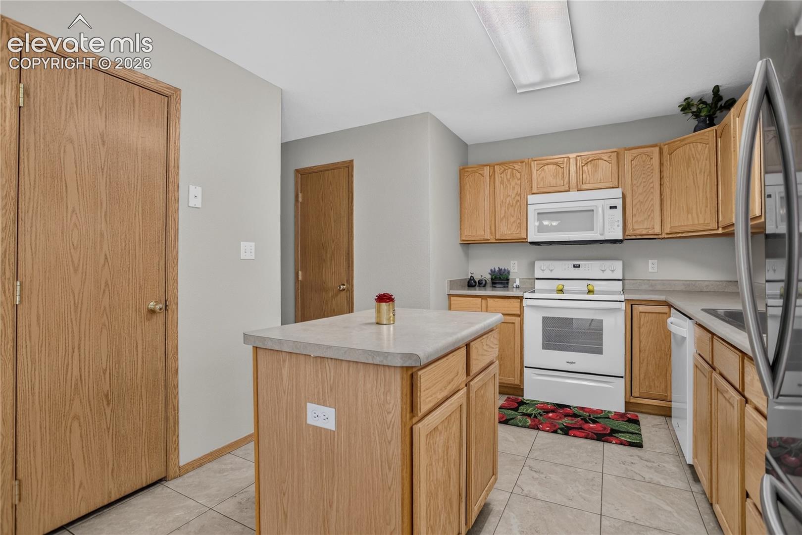 Kitchen featuring light wood cabinetry, white appliances, a center island with a light-toned countertop, and tiled flooring