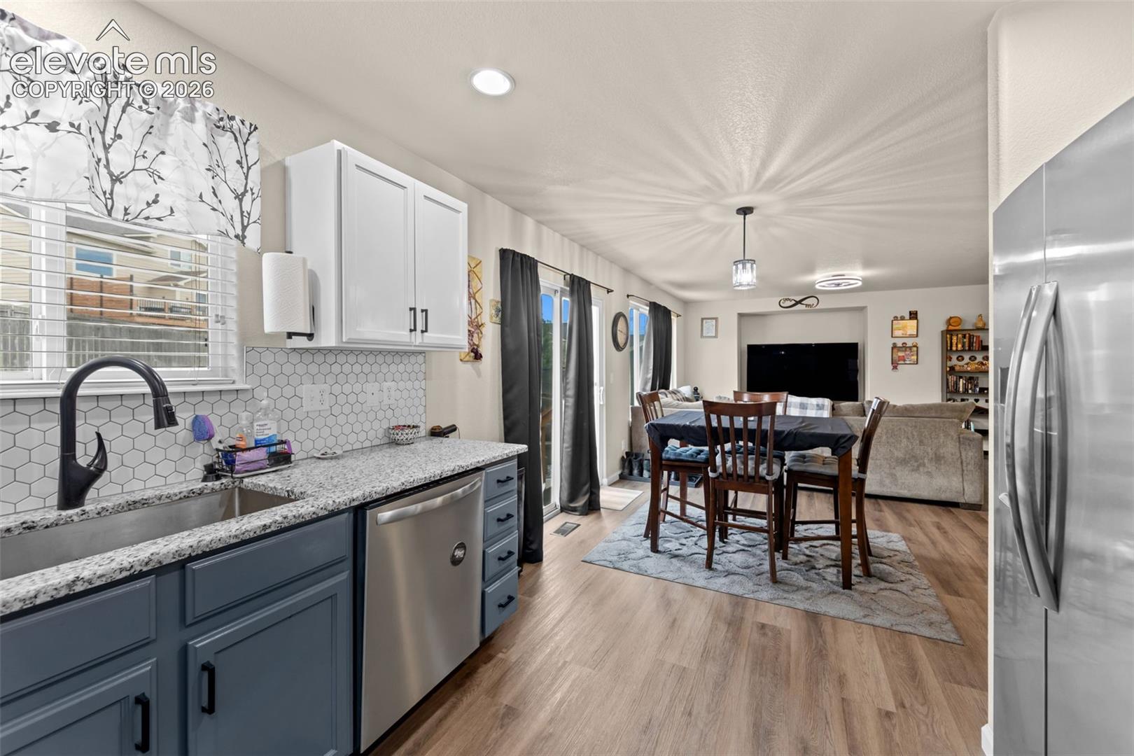 Open-concept kitchen and dining area featuring a hexagonal tile backsplash, granite-style countertops, stainless steel appliances, and wood-finish flooring