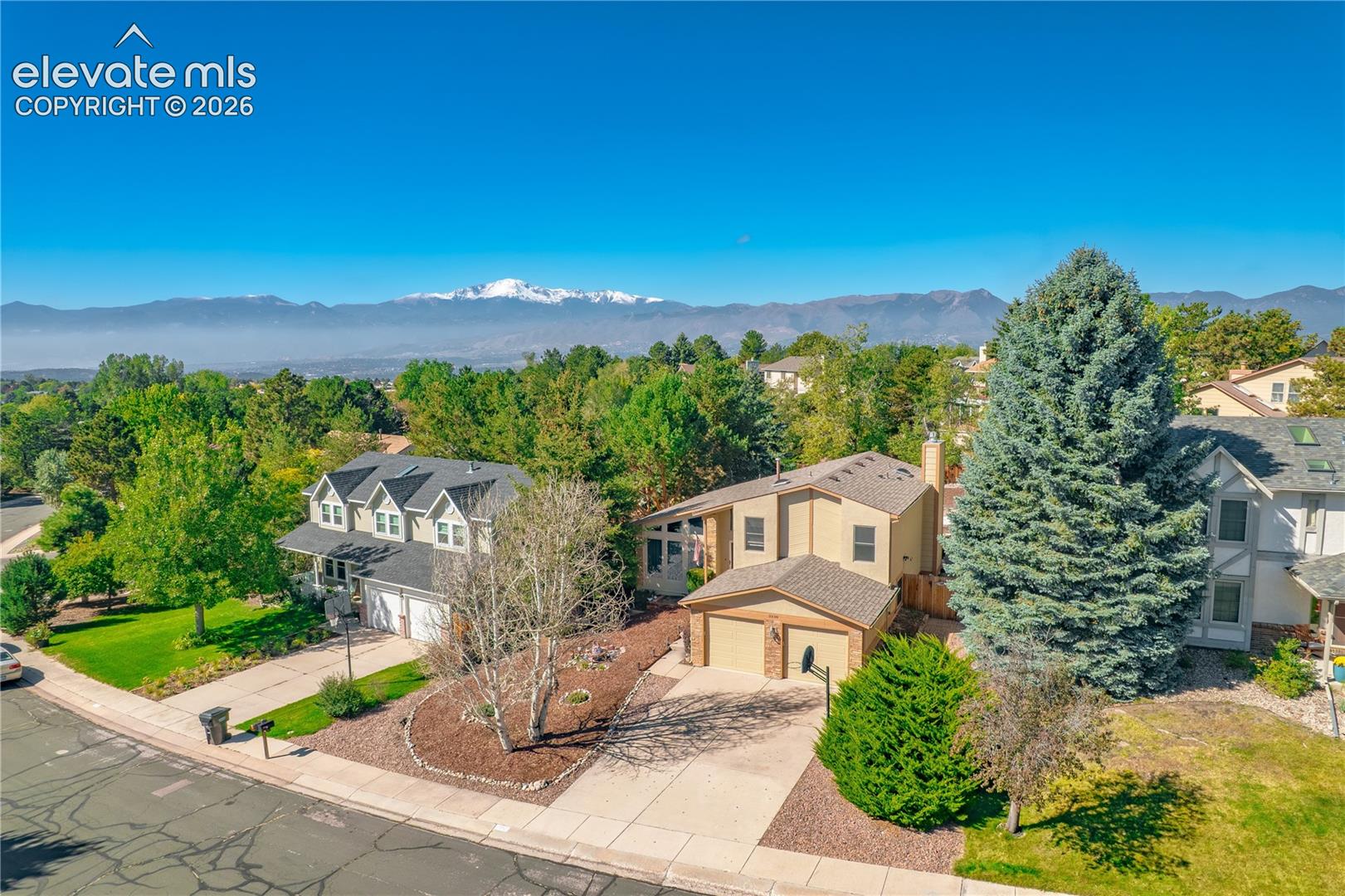 Aerial perspective showcasing multiple properties, with a prominent two-story residence featuring a front-facing two-car garage