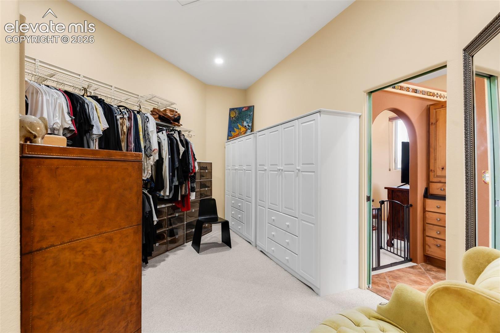 Walk-in closet featuring white built-in cabinetry with integrated drawers and shelving, wall-mounted tiered rack system, and neutral carpeting