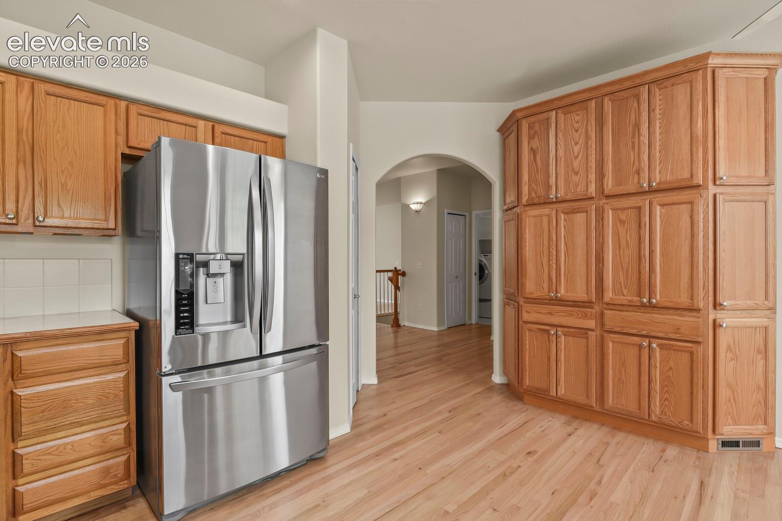 Kitchen featuring custom floor-to-ceiling cabinetry, stainless steel french-door refrigerator, arched doorway, and wood-finish flooring