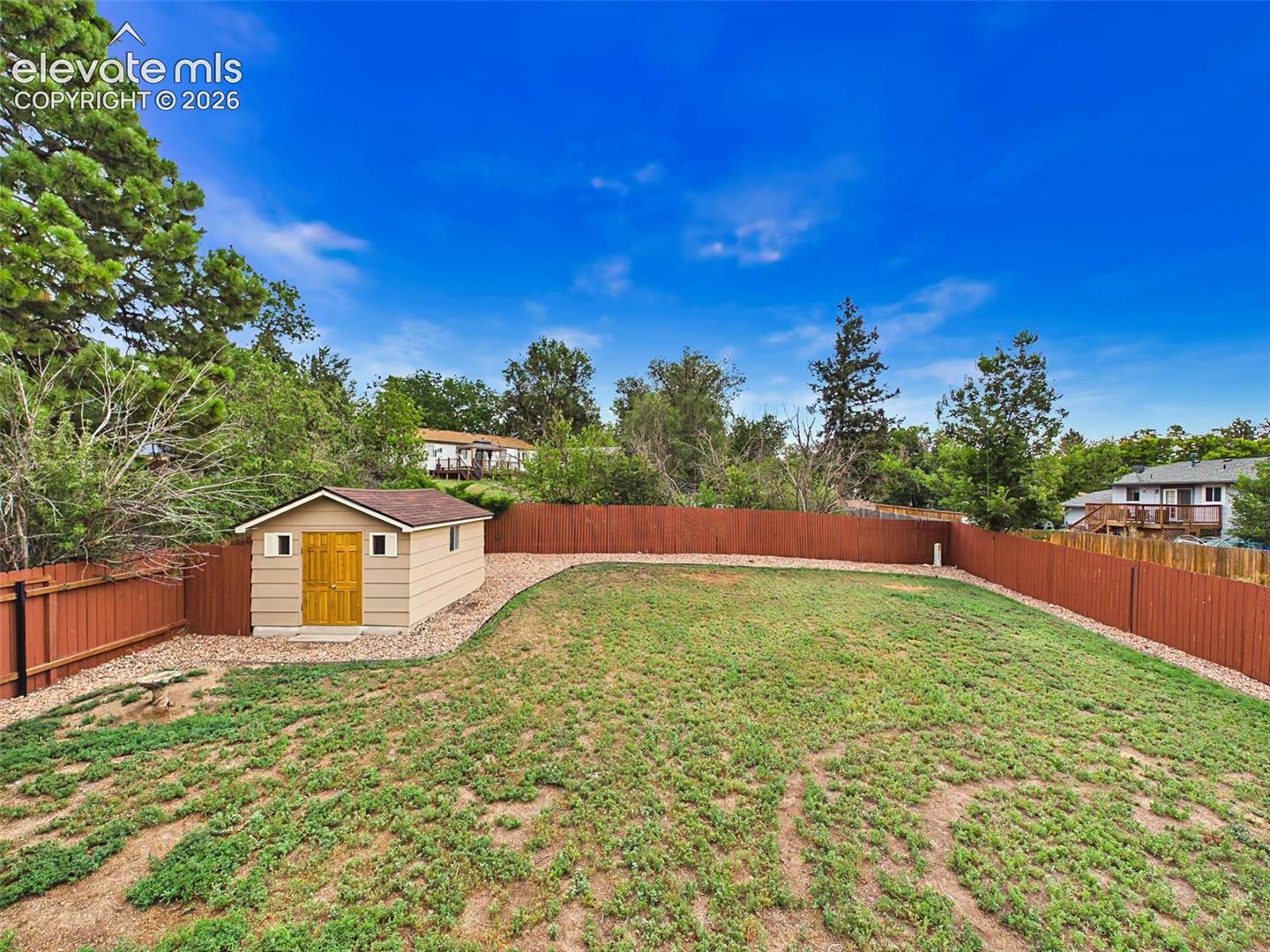 Another view showcases the generous yard size, low-maintenance rock borders, and detached storage shed.