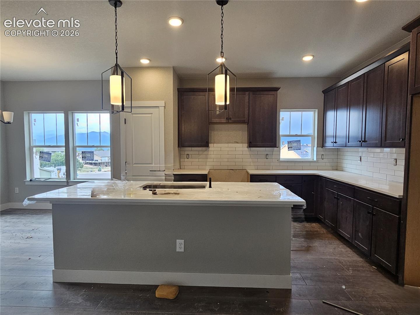 kitchen with center island, pendant lights, dark upper cabinets, subway tile backsplash, and windows showing an exterior view