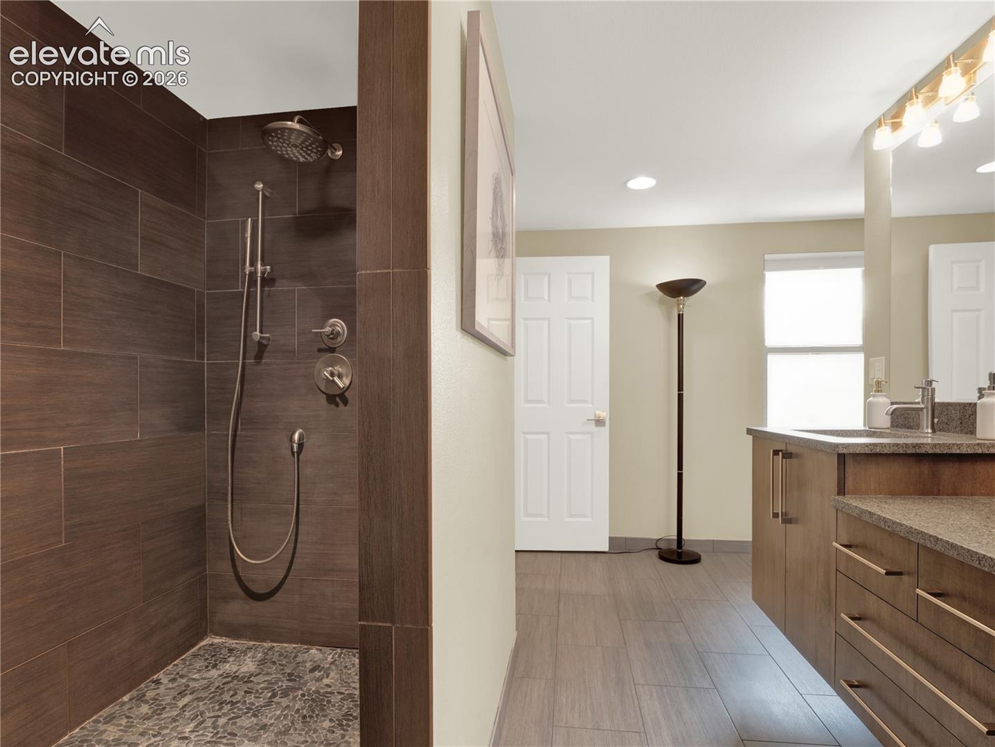 Walk-in shower with dark horizontal tile, stone-textured floor, and chrome fixtures, paired with a floating vanity featuring a stone countertop and minimalist cabinetry