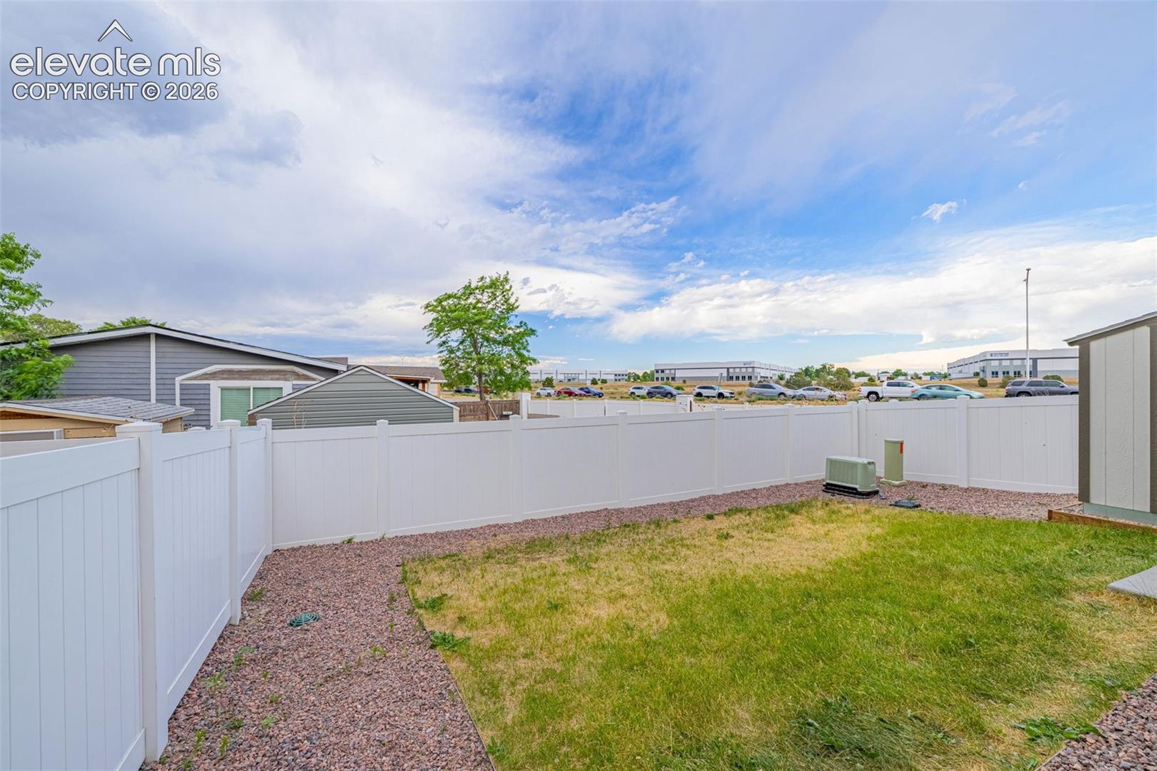 Private backyard featuring a white privacy fence, a patch of green lawn, and a gravel border