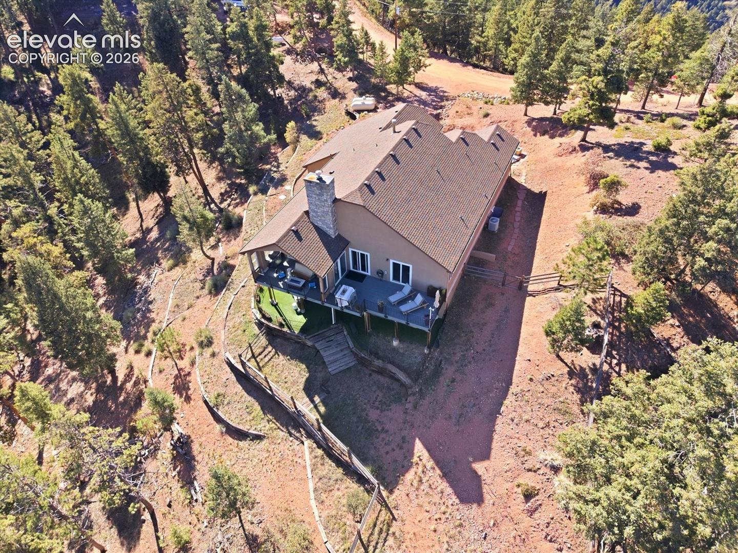 Multi-level residence featuring a stone-clad exterior chimney, expansive raised deck, and a forested hillside setting