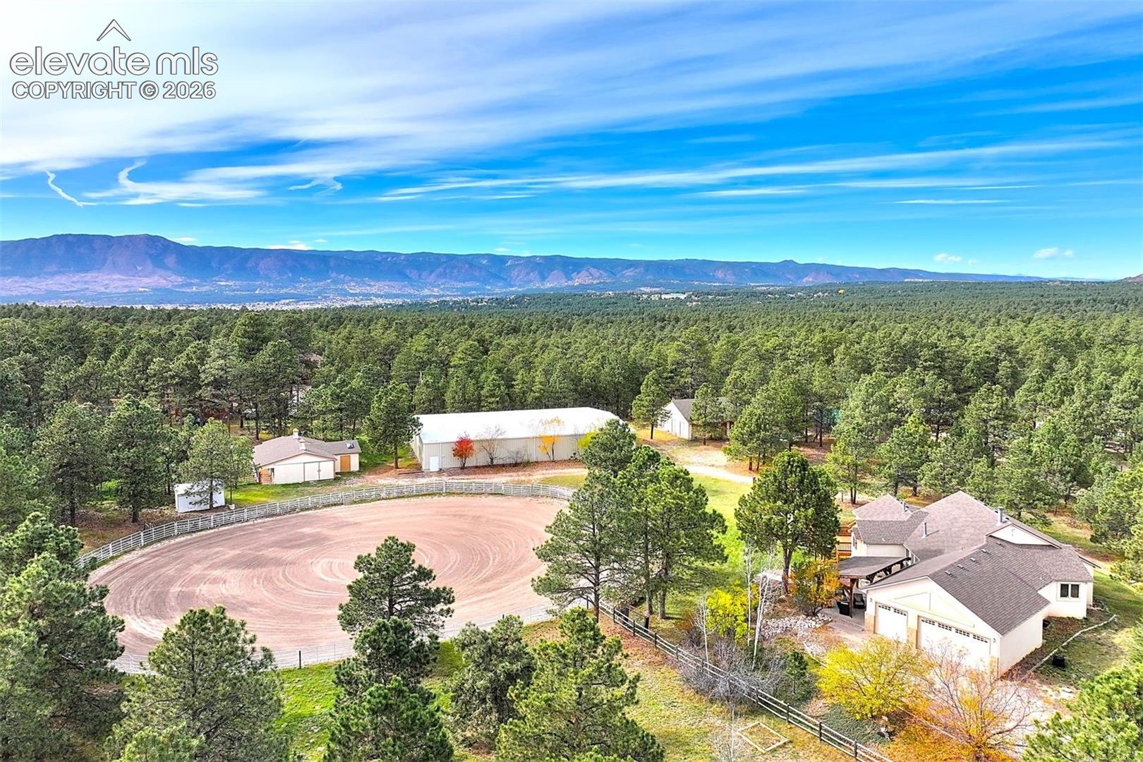 Aerial property featuring a circular equestrian arena, indoor riding arena, 4-stall barn, workshop/outbuilding