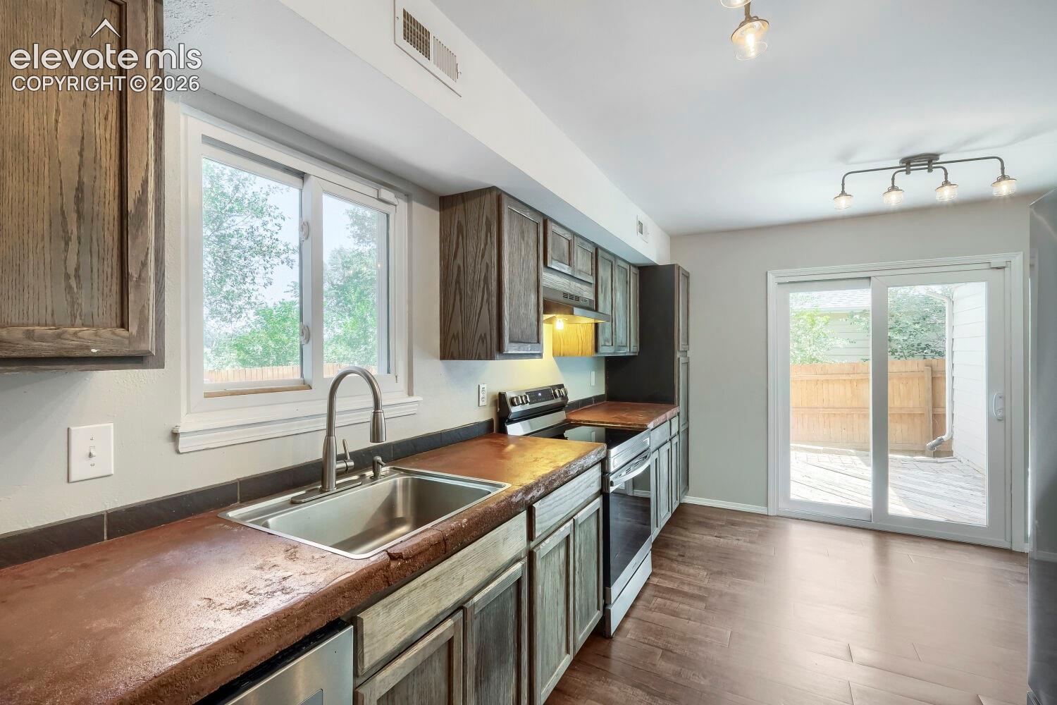 Kitchen featuring wood-finish flooring, dark wood cabinetry, a stainless steel sink with a gooseneck faucet, and a sliding glass door leading to an outdoor deck