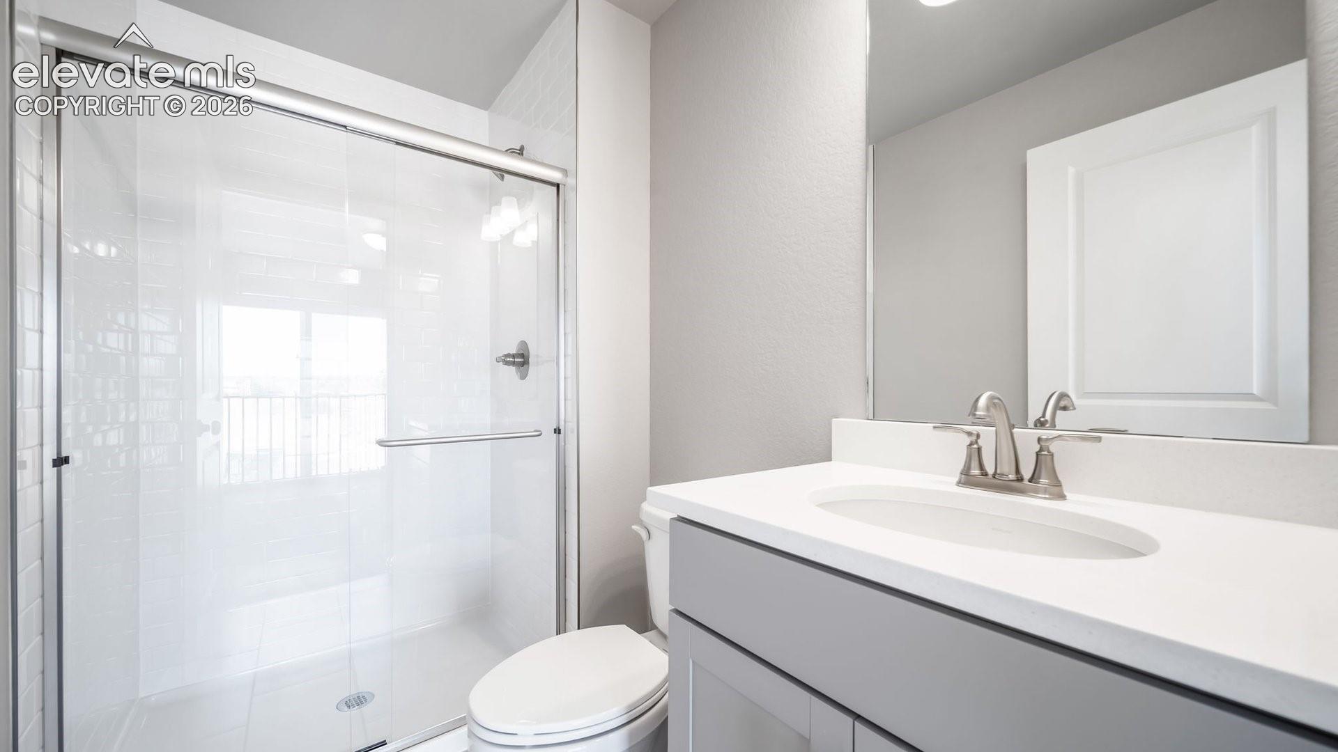 Bathroom featuring a vanity with a white solid-surface countertop and integrated oval sink, chrome dual-handle faucet, full-width mirror, and a walk-in shower with a glass enclosure and chrome hardware
*photos of a model home*