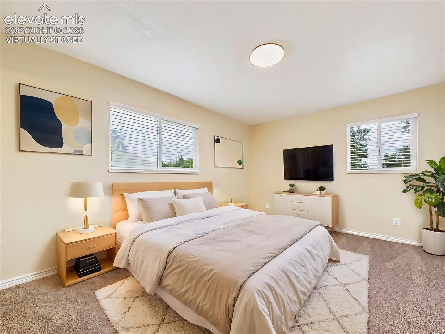 (Virtually Staged) Spacious primary bedroom featuring soft carpeting, large windows, and plenty of room for a king-size bed and additional furnishings.