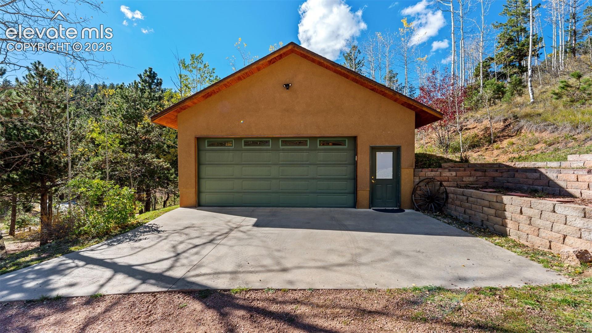 Detached structure featuring a stucco exterior, concrete driveway, multi-pane sectional garage door, private access door, and tiered stone retaining wall