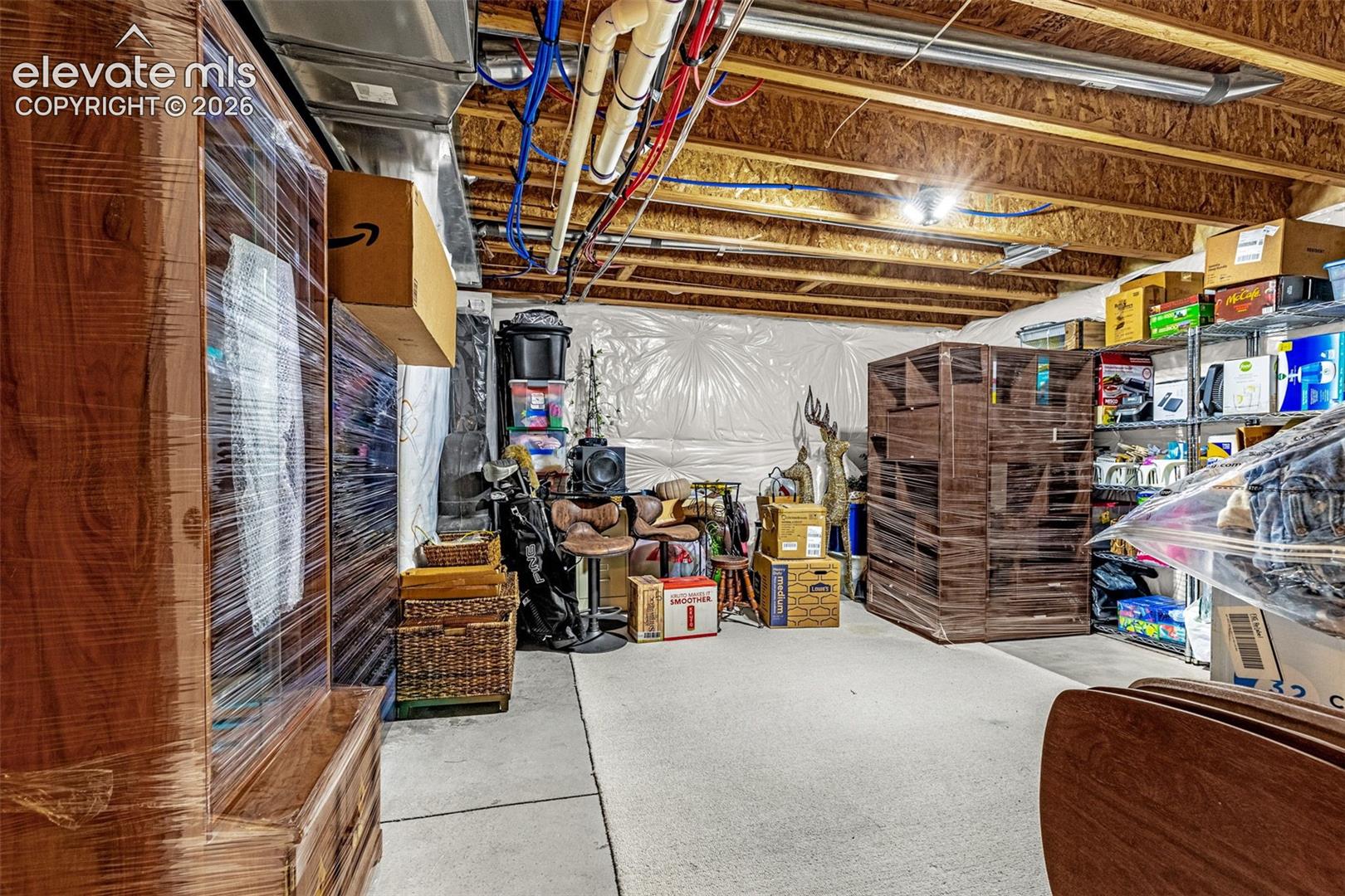 Unfinished storage space featuring exposed wooden floor joists, concrete flooring, and vapor-barrier wall coverage