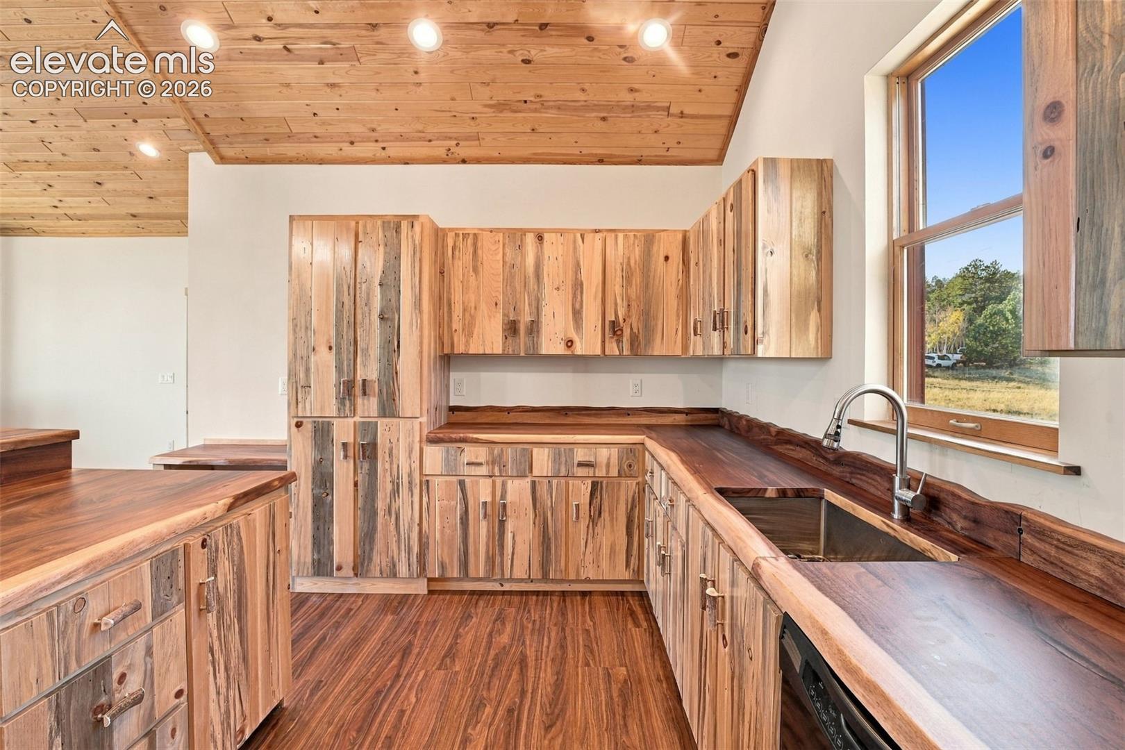 Custom cabinetry featuring natural wood grain finishes, live-edge wood countertops, recessed ceiling lighting, wood-plank ceiling treatment, and wood-finish flooring