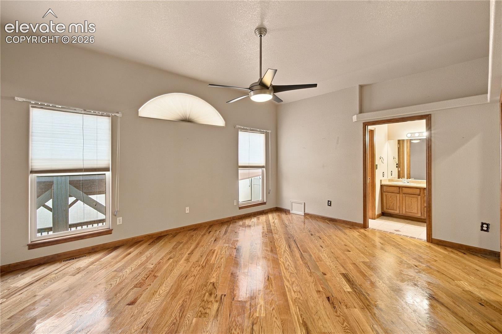 Room featuring wood-finish flooring, vaulted ceiling with integrated light fixture and ceiling fan, arch-top window, and wood cabinetry in the attached space